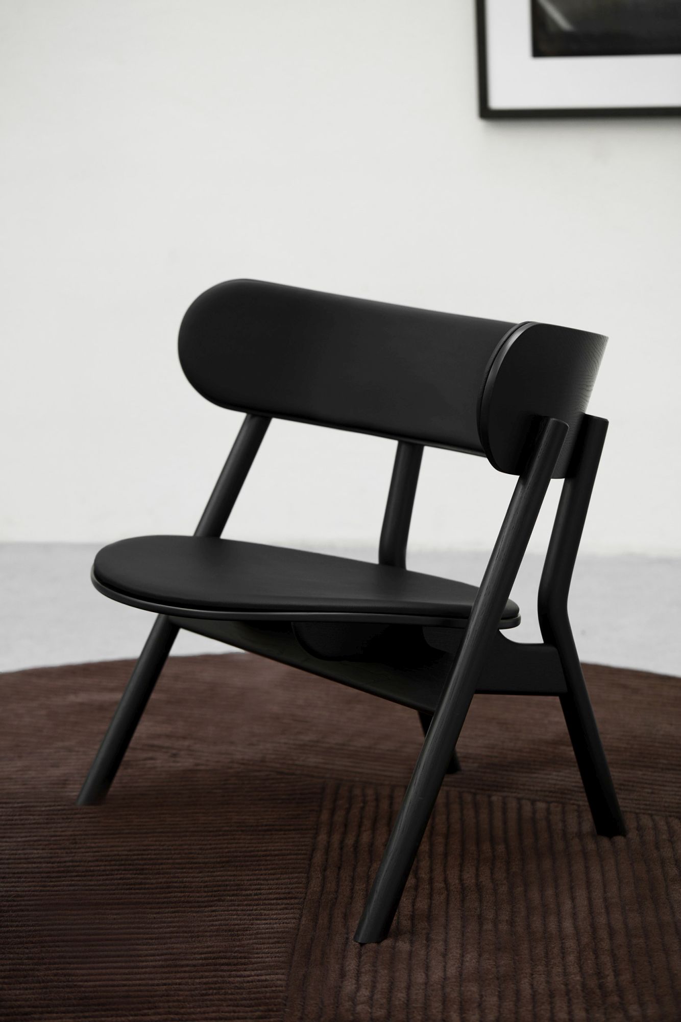 Schwarzer Oaki Lounge Chair mit Polsterung auf braunem Teppich, modernes Möbeldesign für Wohnzimmer und Büro.