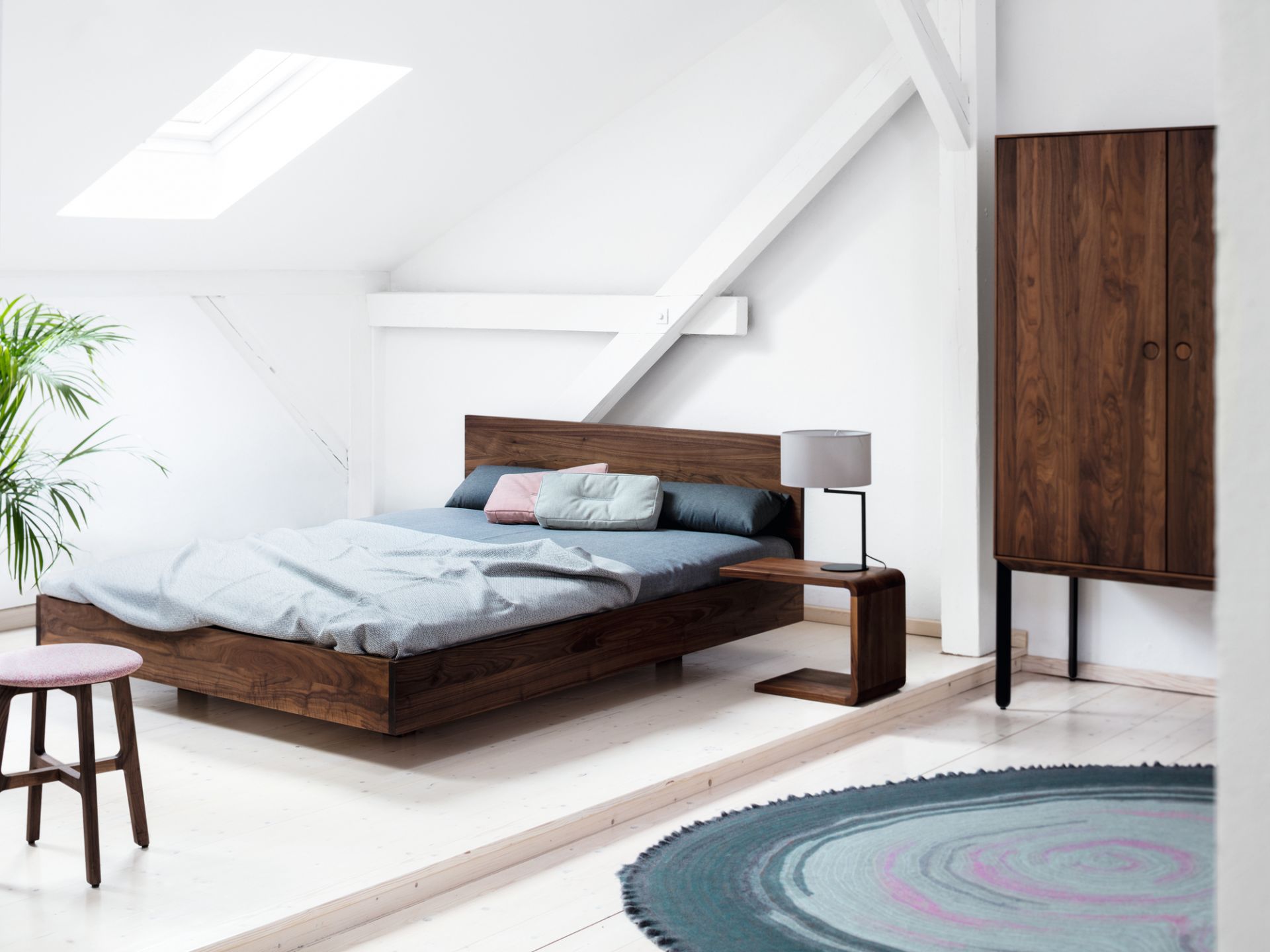 Schlafzimmer mit modernem Holzbett, Nachttisch, Kleiderschrank und Teppich in einem hellen Dachgeschoss.