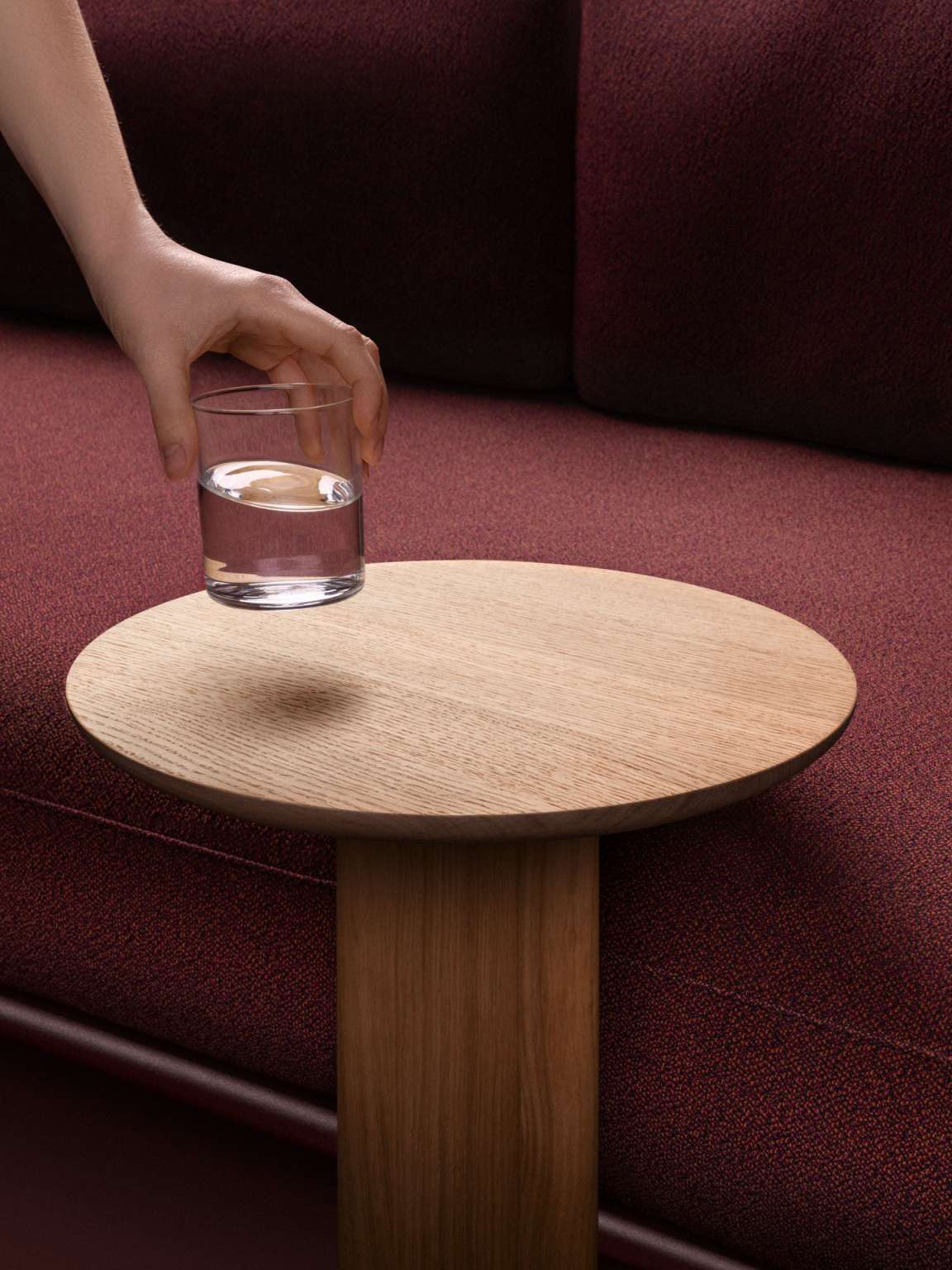 Anagram Beistelltisch von Vitra, runde Tischplatte aus Eichenholz, Hand stellt ein Wasserglas darauf ab.