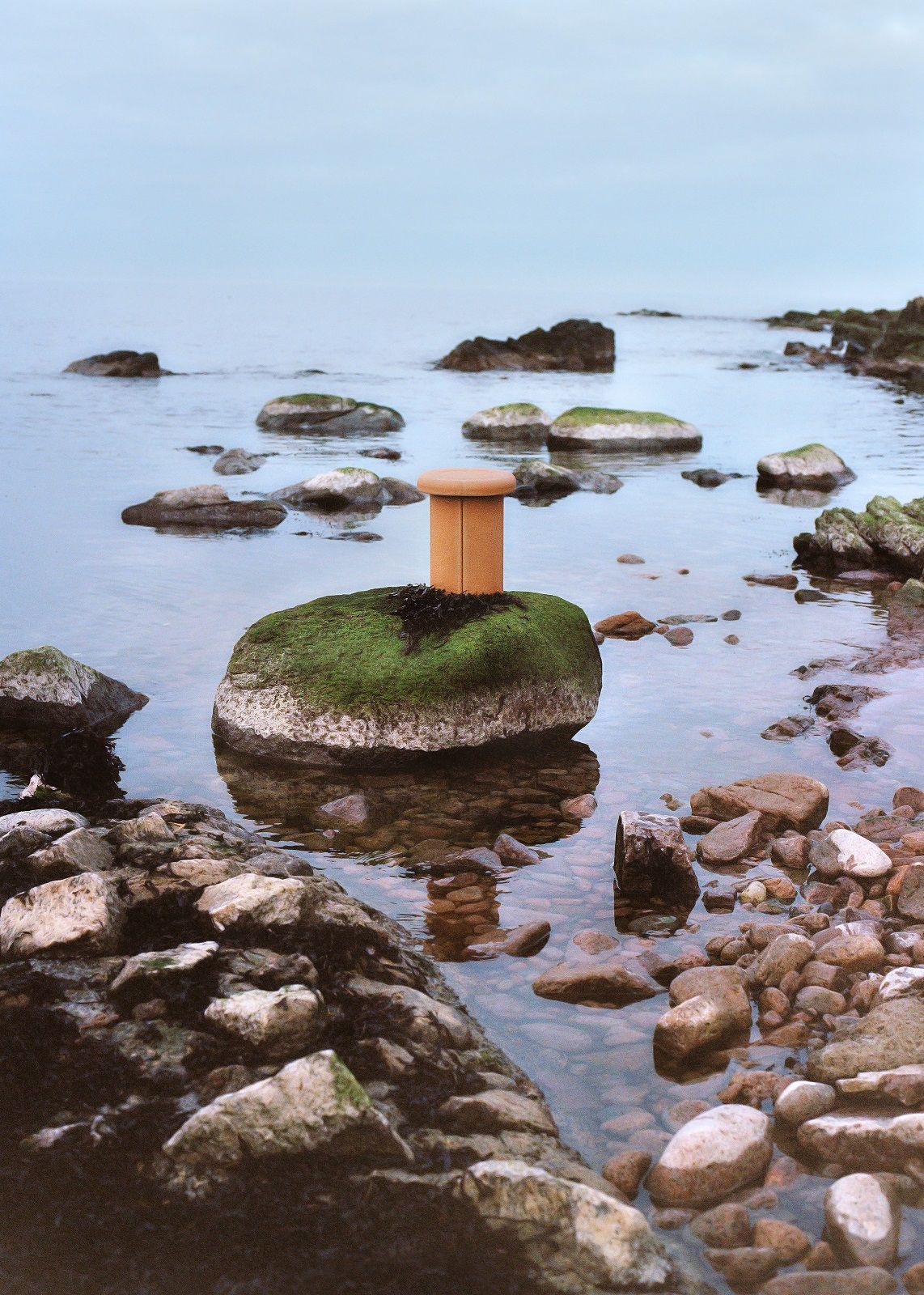 Alder Stool Hocker von Mater, Outdoor-Möbel auf einem moosbewachsenen Stein im Wasser.