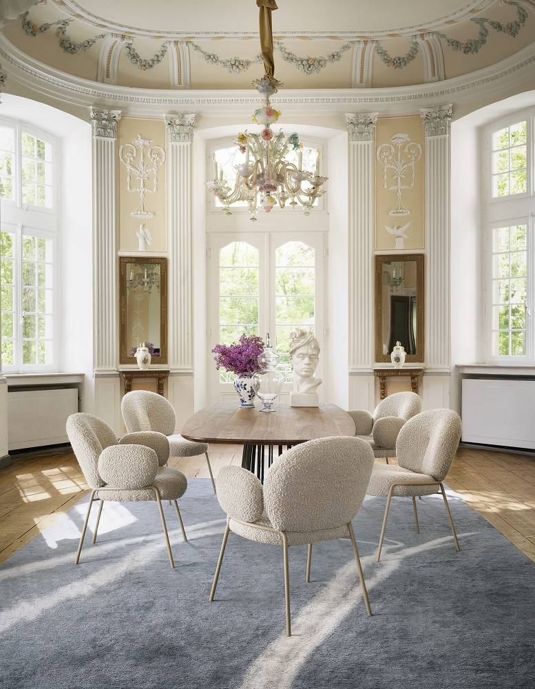 Esszimmer mit ovalem Holztisch und sechs beigen Bouclé-Stühlen auf blauem Teppich. Luxuriöses Interieur.
