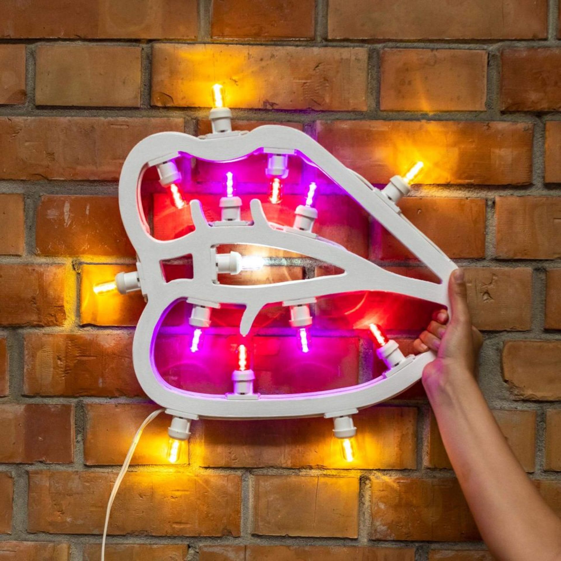 Weiße Lippen Neon Wanddeko mit gelben und pinken Lichtern vor einer Backsteinmauer. Moderne LED Leuchte.