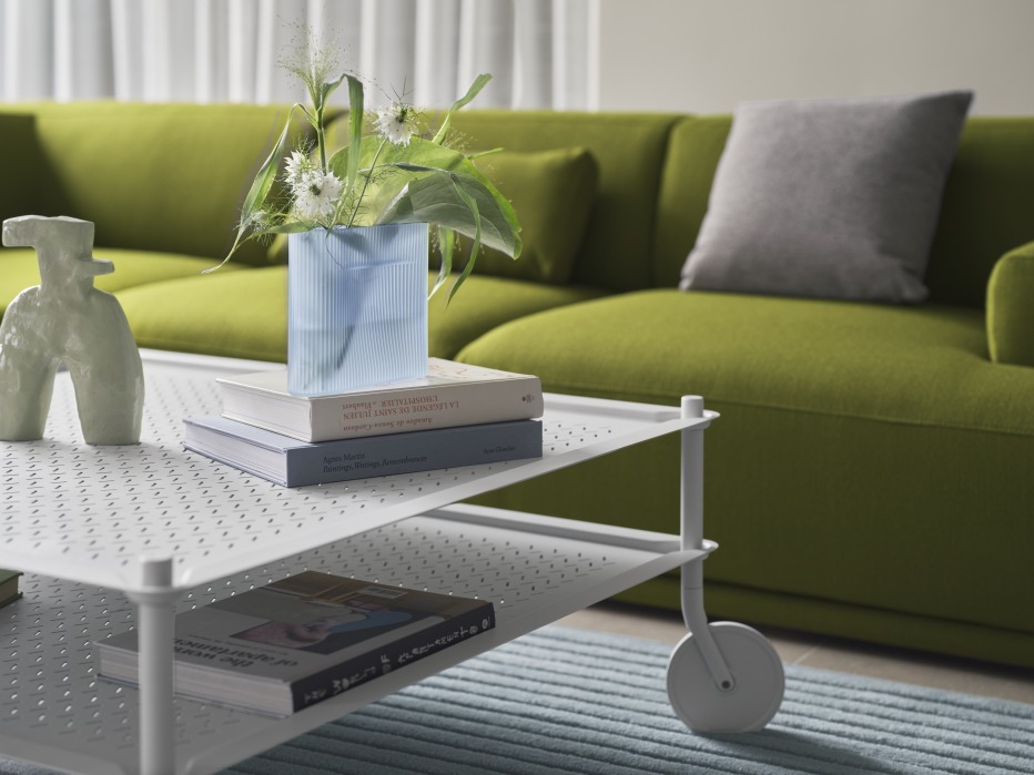 Muuto Flow Coffee Table: Weißer Couchtisch auf Rollen mit zwei Ablageflächen vor grünem Sofa.