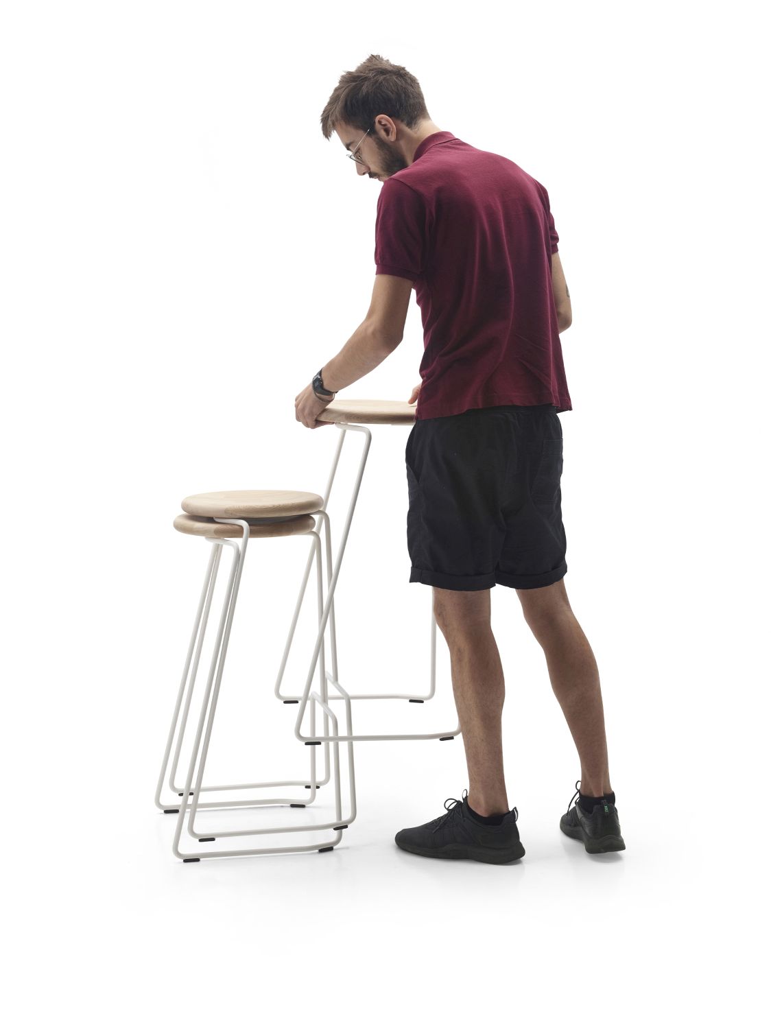 Mann betrachtet zwei Tiki Hocker von Extremis, moderne Barhocker für den Outdoor-Bereich mit Holzsitzen.