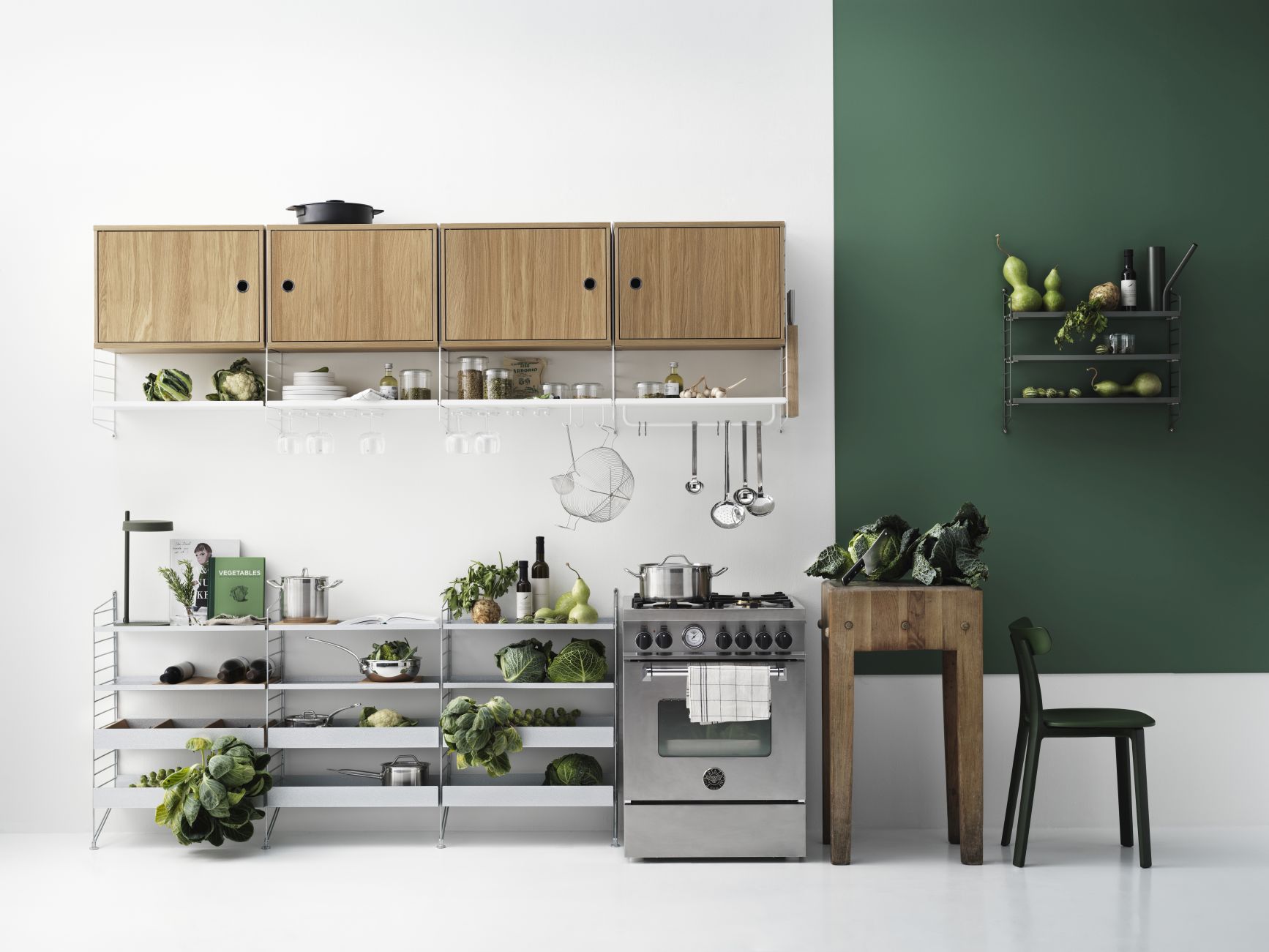 Helle Küche mit String Regalsystem, Holzschränken, Edelstahlherd und frischem Gemüse für eine gesunde Ernährung.