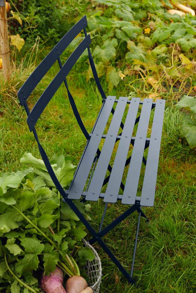 Fermob Bistro Klappbank für zwei Personen in Dunkelblau, Gartenmöbel für den Außenbereich, Detailaufnahme im Grünen.