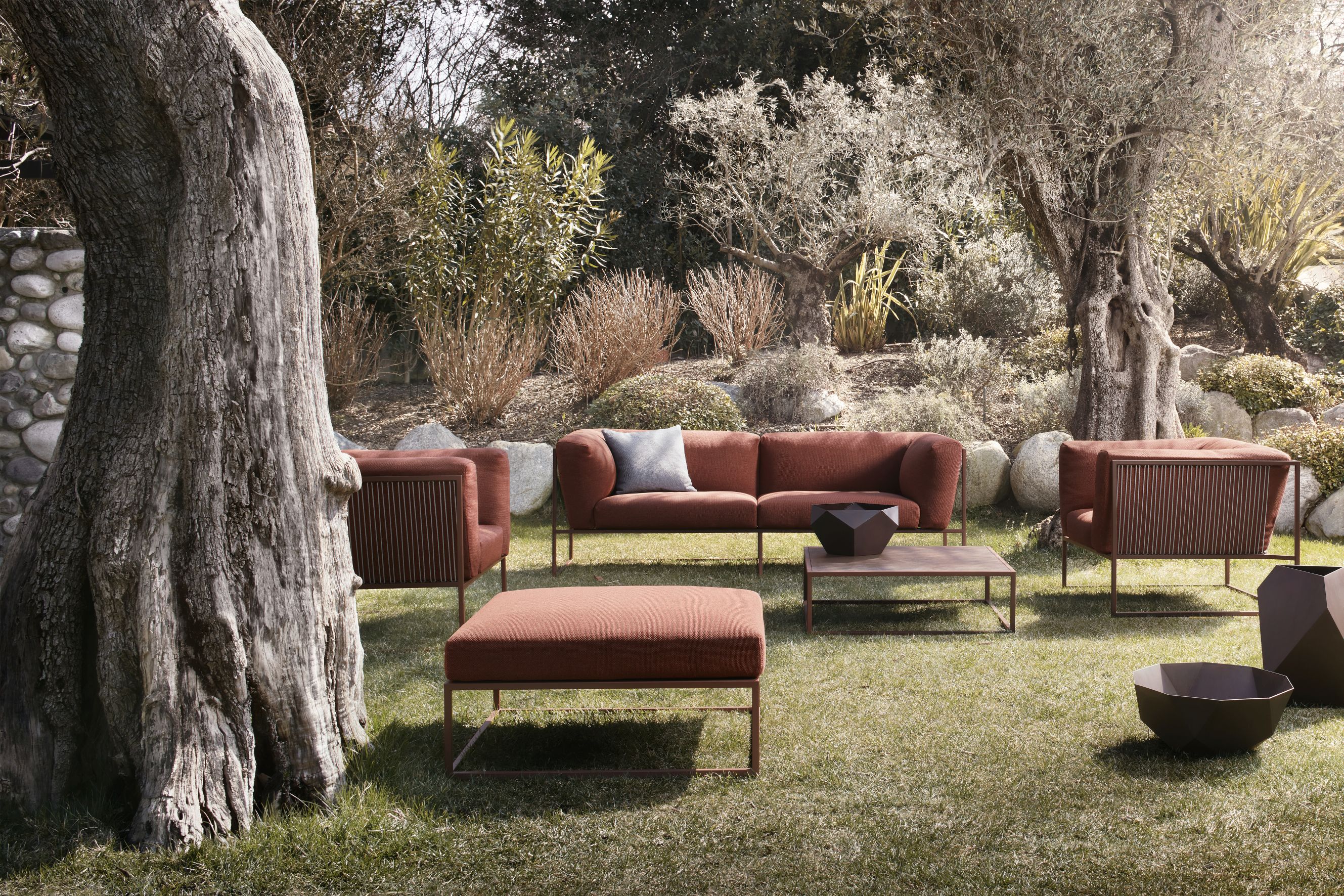 Arpa Outdoor Sessel von MDF Italia in Rostrot auf Rasen mit Lounge Möbeln und Gartendeko.