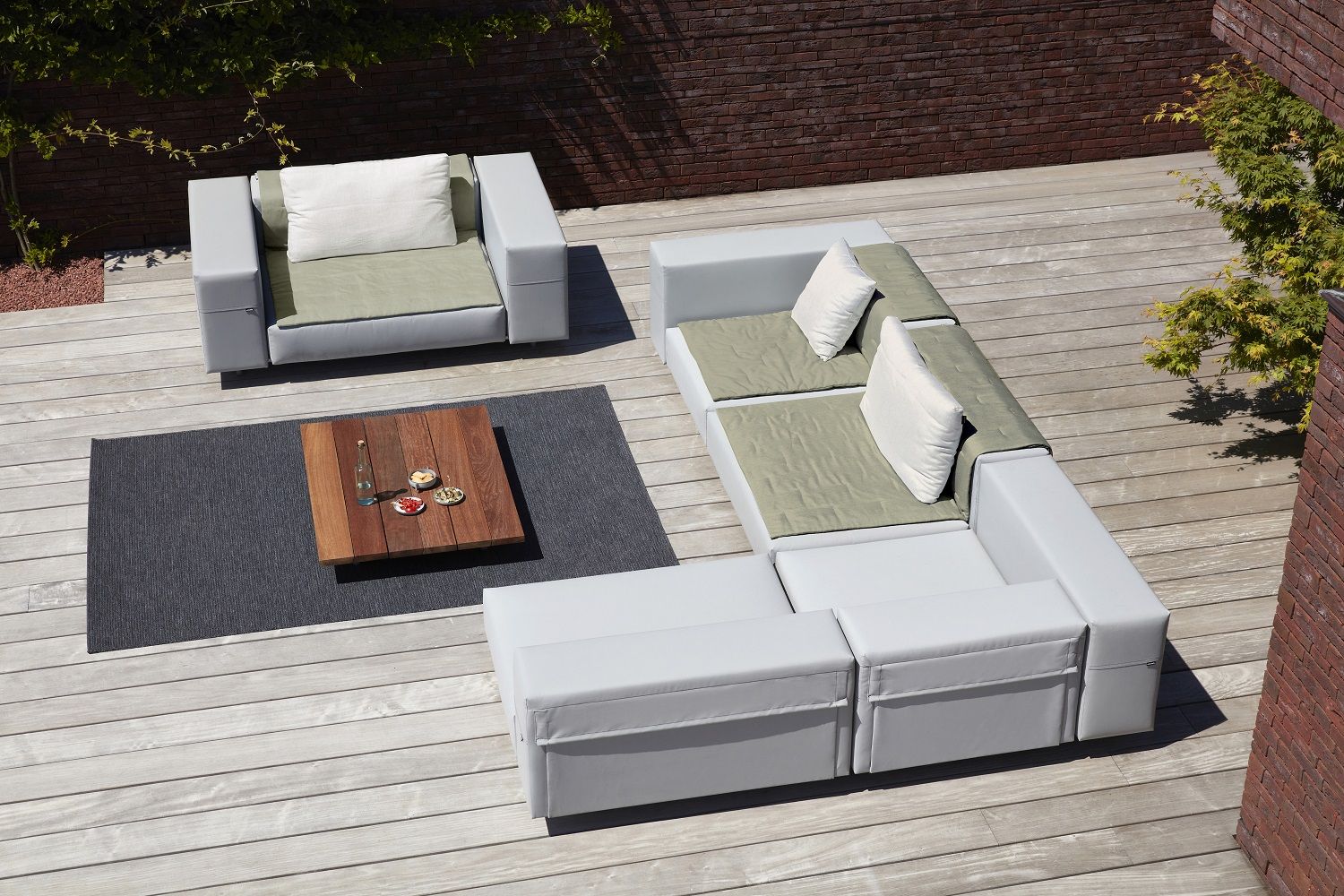 Walrus Outdoor Club Sessel von Extremis als modulares Lounge-Set auf einer Holzterrasse mit Teppich.
