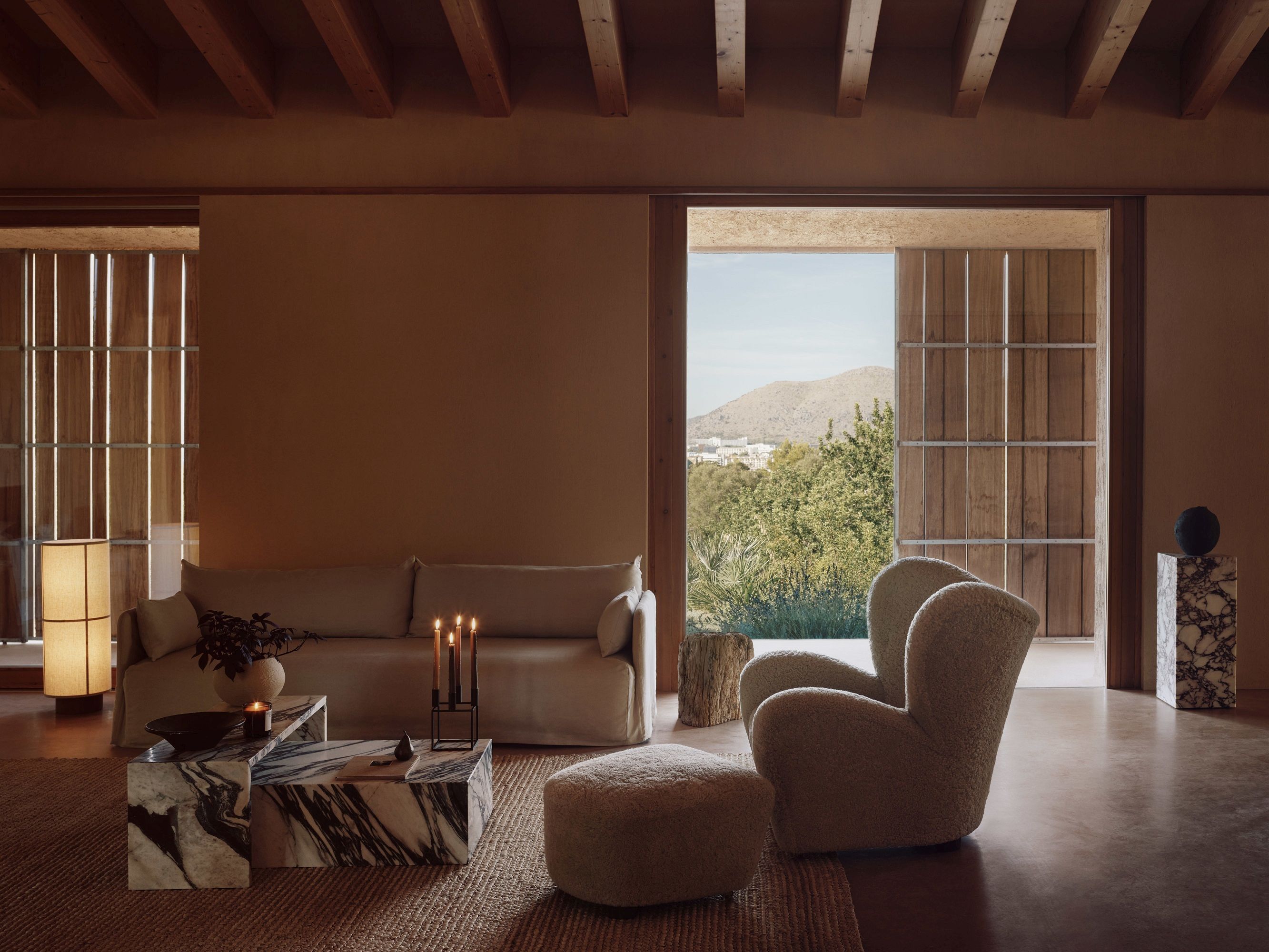 Helles Wohnzimmer mit Audo Copenhagen Offset Sofa, Sessel und Marmor-Couchtisch vor malerischer Landschaft.