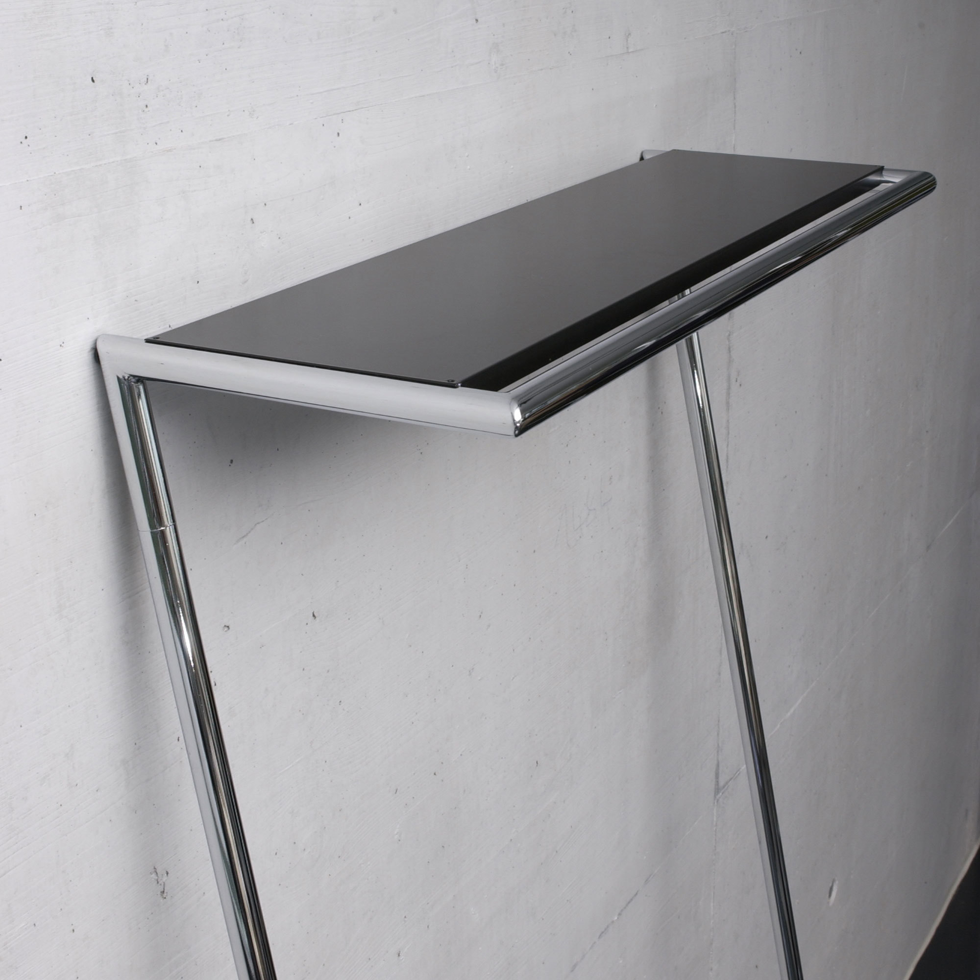 Hutablage für Zen Garderobe: Schwarze Ablage mit verchromtem Gestell vor einer Wand.