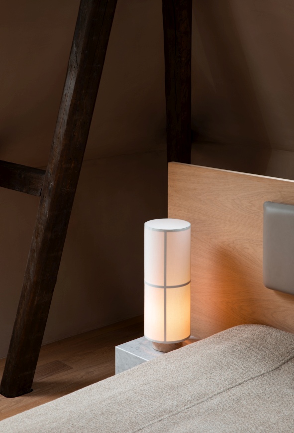 Audo Hashira Tischleuchte auf Nachttisch, zylindrisches Design mit Stoffschirm und warmem Licht.