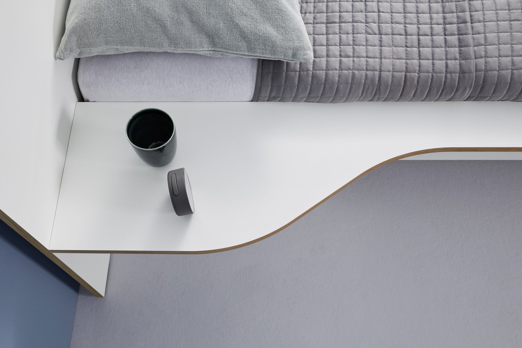 Detailaufnahme vom Plane Doppelbett von Müller Möbelwerkstätten mit Nachttisch, Lampe und Tasse.