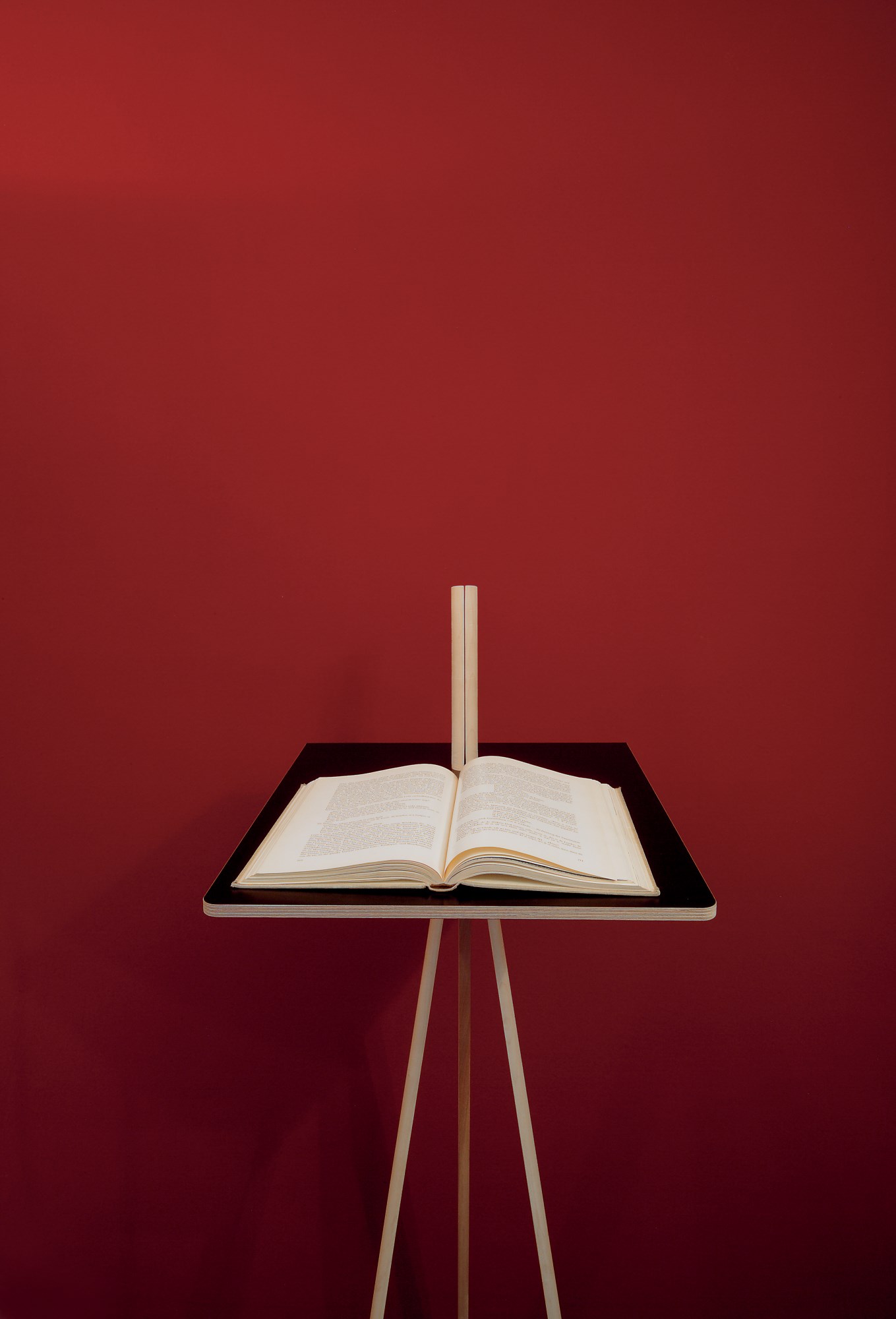 Der kleine Lehner Stehpult von Nils Holger Moormann mit aufgeschlagenem Buch vor roter Wand.