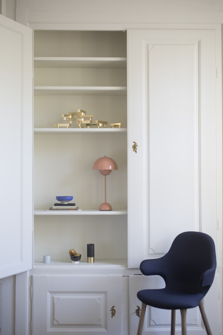 AndTradition Catch Chair JH1 Stuhl in dunklem Blau vor weißem Schrank mit Deko-Elementen.