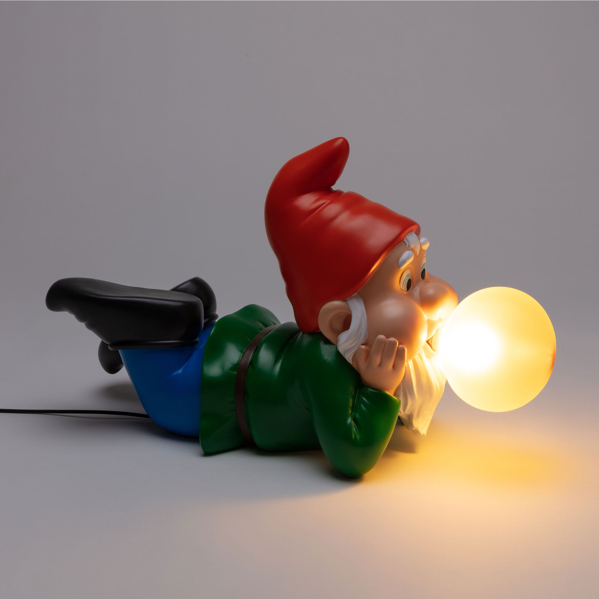 Seletti Gummy Dreaming Leuchte: Liegender Gartenzwerg mit roter Mütze und leuchtender Kugel als Lampe.