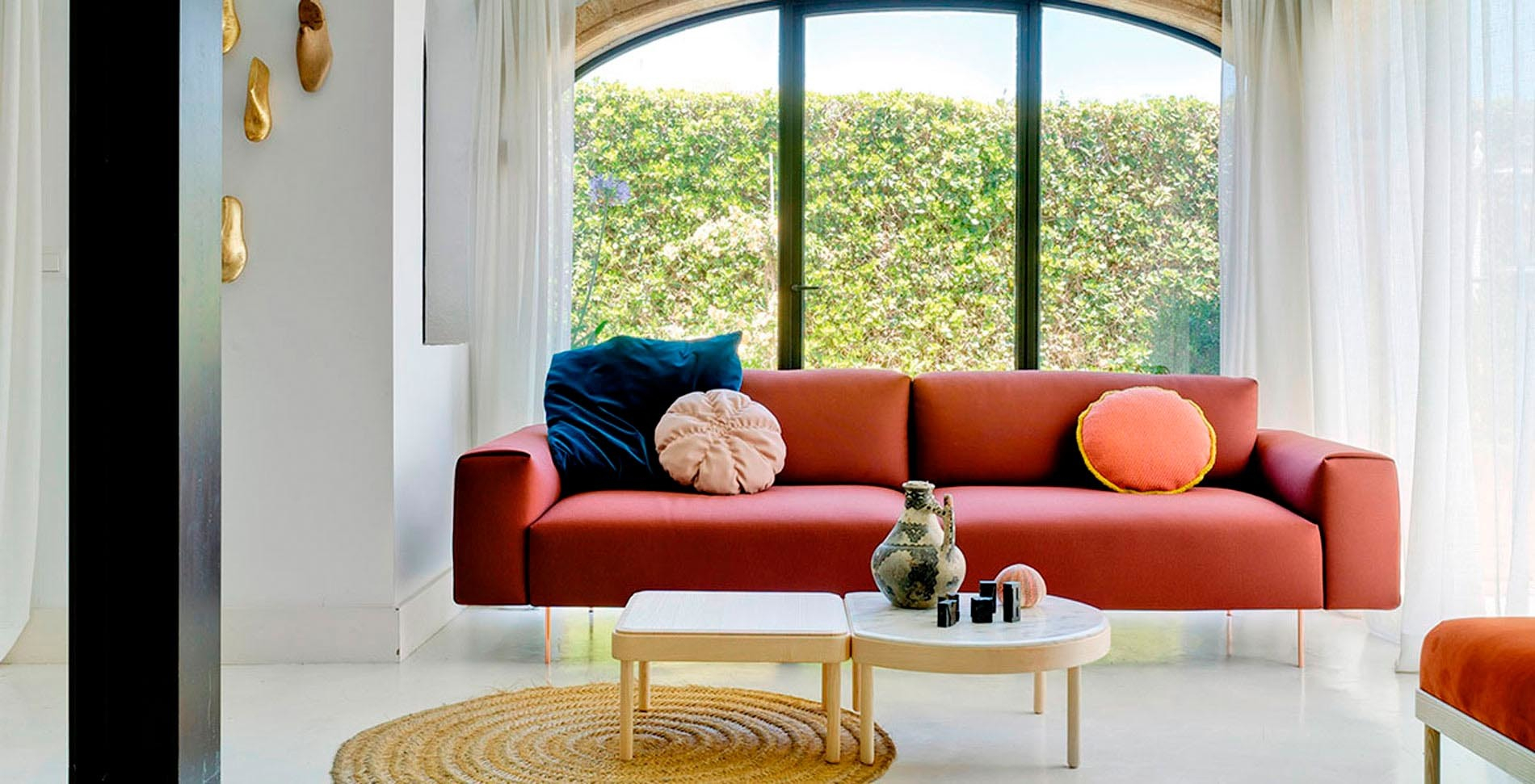 Tip Toe Sofa von Sancal in Terrakotta mit Zierkissen und Beistelltischen vor Fenster.
