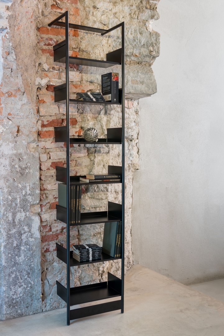 Schwarzes Pool Anlehnregal von Mox, Medium, vor einer Backsteinwand, mit Büchern und Dekoartikeln.