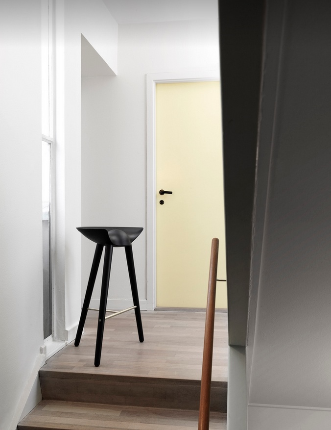 Schwarzer ML42 Barhocker von Audo auf Holztreppe vor gelber Tür, minimalistisches skandinavisches Design.