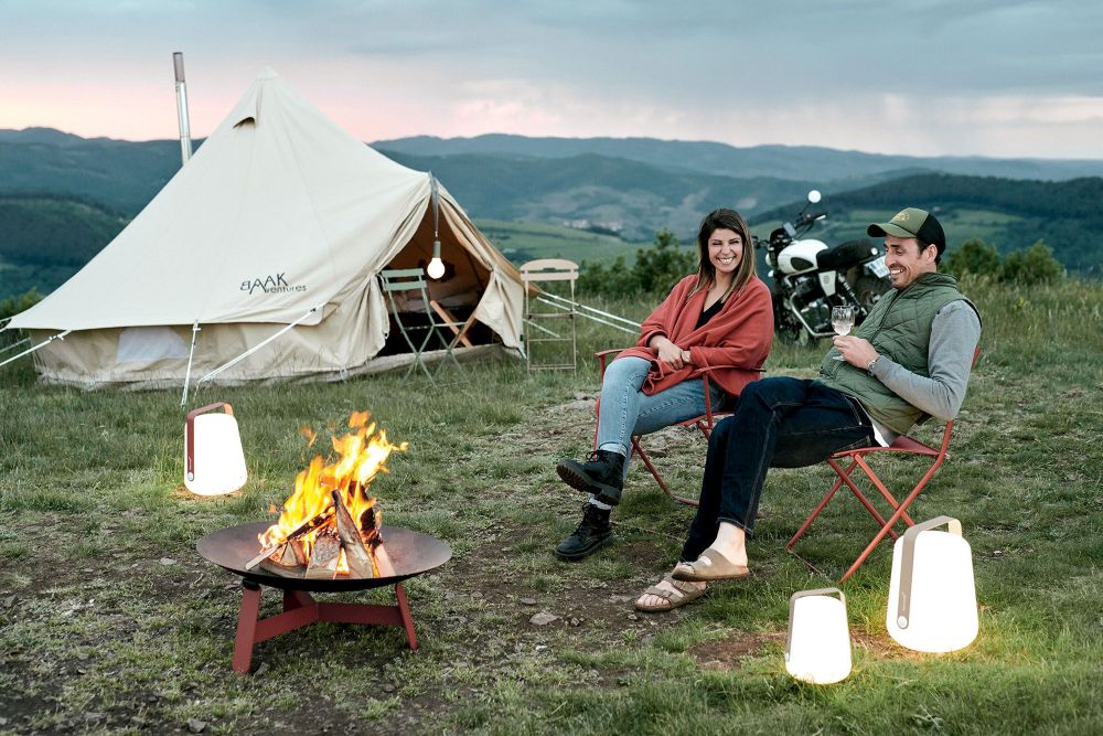 Zwei Personen sitzen auf roten Fermob Stühlen am Lagerfeuer, Camping mit Plein Air Stühlen.