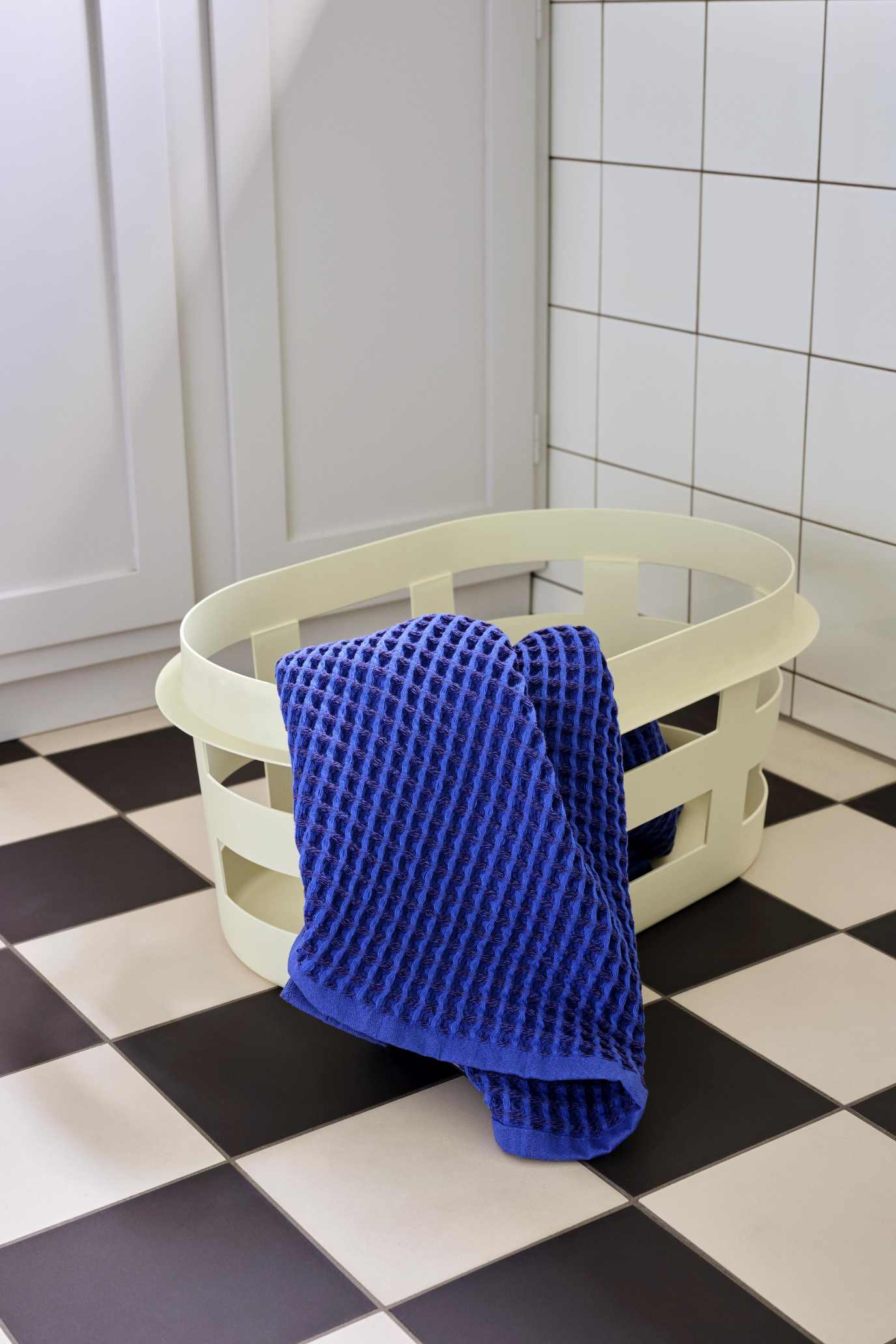 Blauer Frottee-Waschlappen liegt in einem hellen Hay Wäschekorb S RECYCLED auf Schachbrettboden.