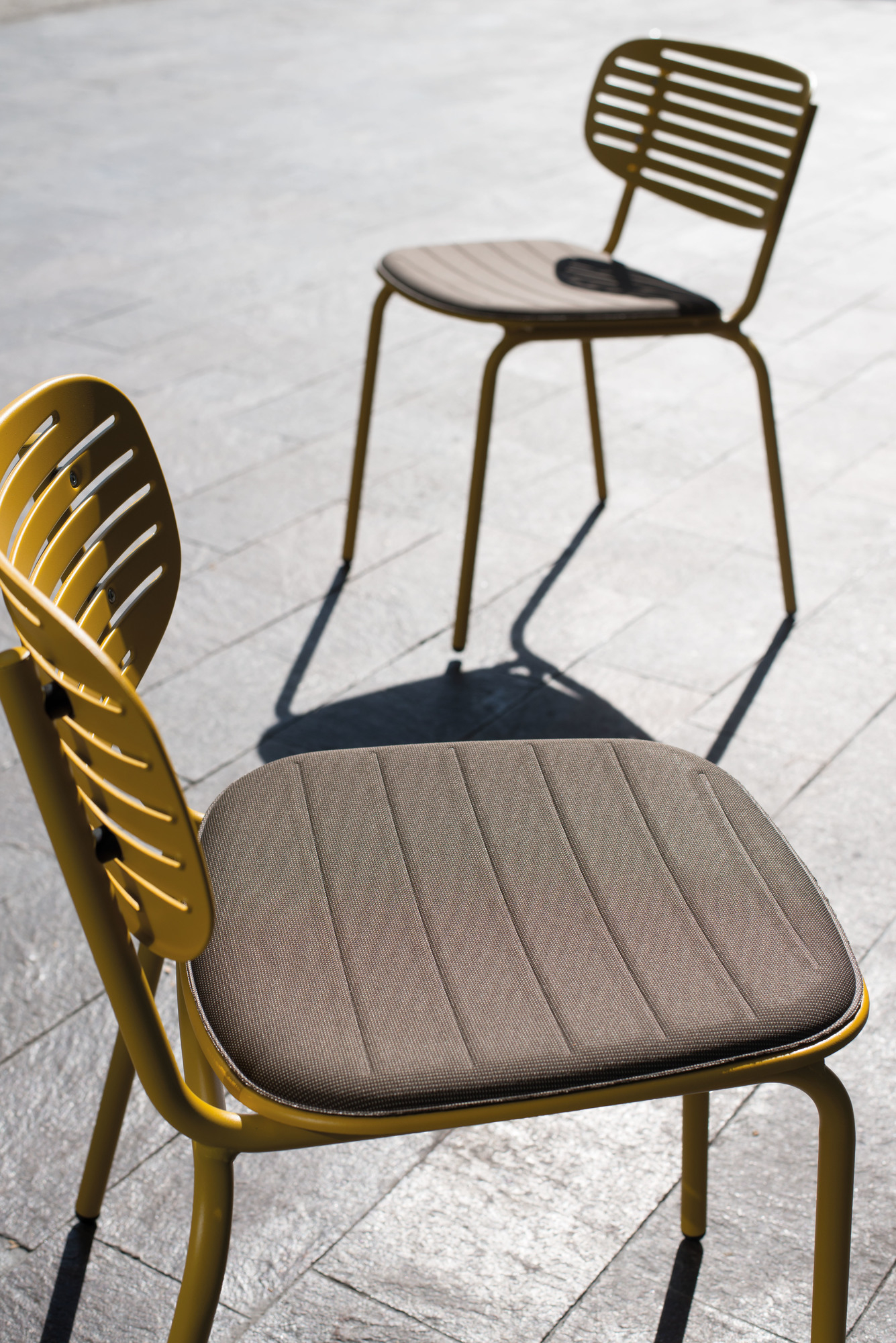 Zwei gelbe Emu Mom Stühle im Freien, Sitzpolster in Braun, modernes Design für Garten und Terrasse.