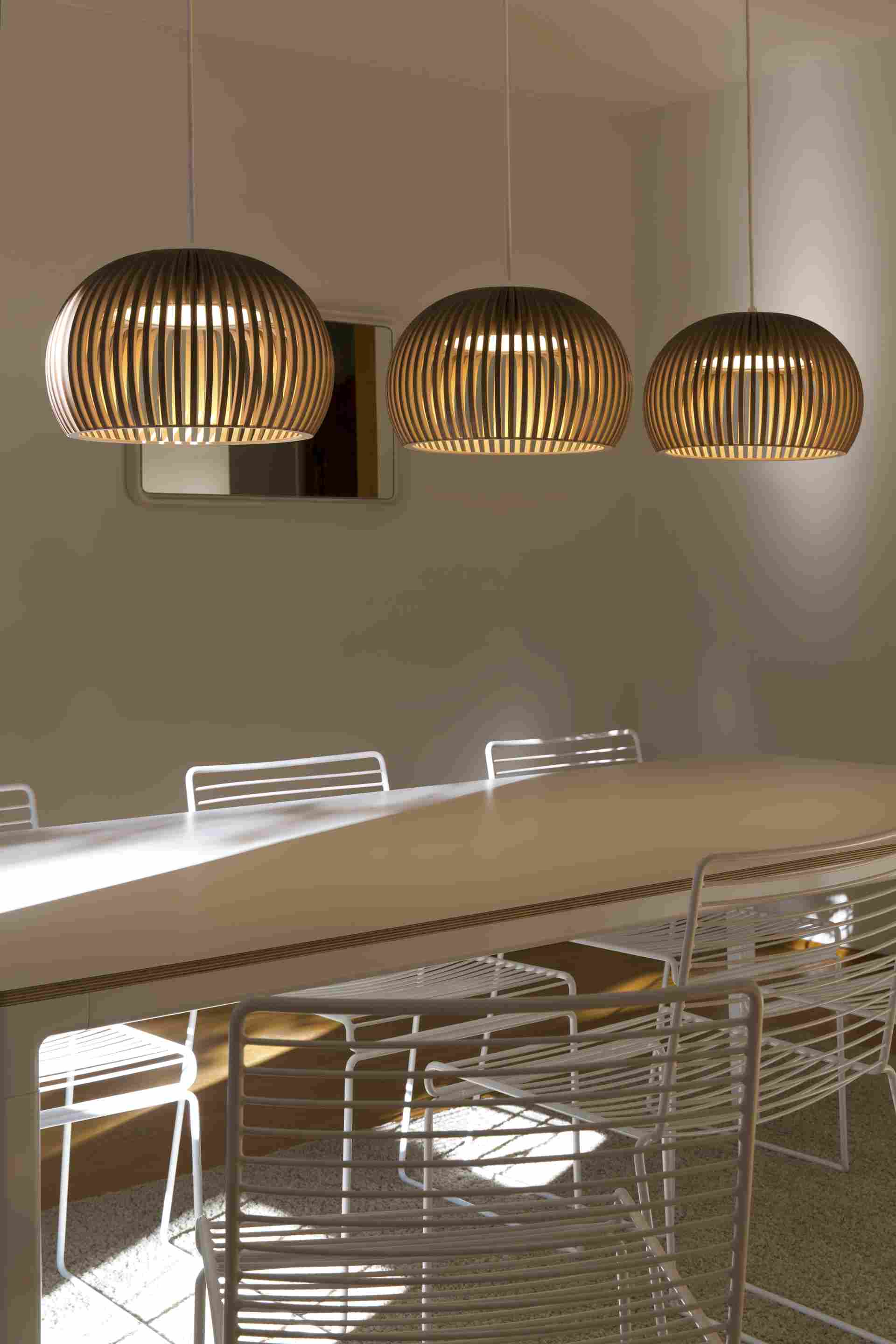 Drei moderne Holz-Pendelleuchten über einem Esstisch mit weißen Stühlen, warmes Licht, stilvolles Design.