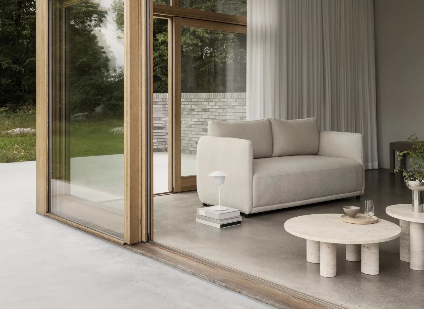 Runder Volos Couchtisch von Blomus aus Travertin im modernen Wohnzimmer mit Sofa und Terrassentür.