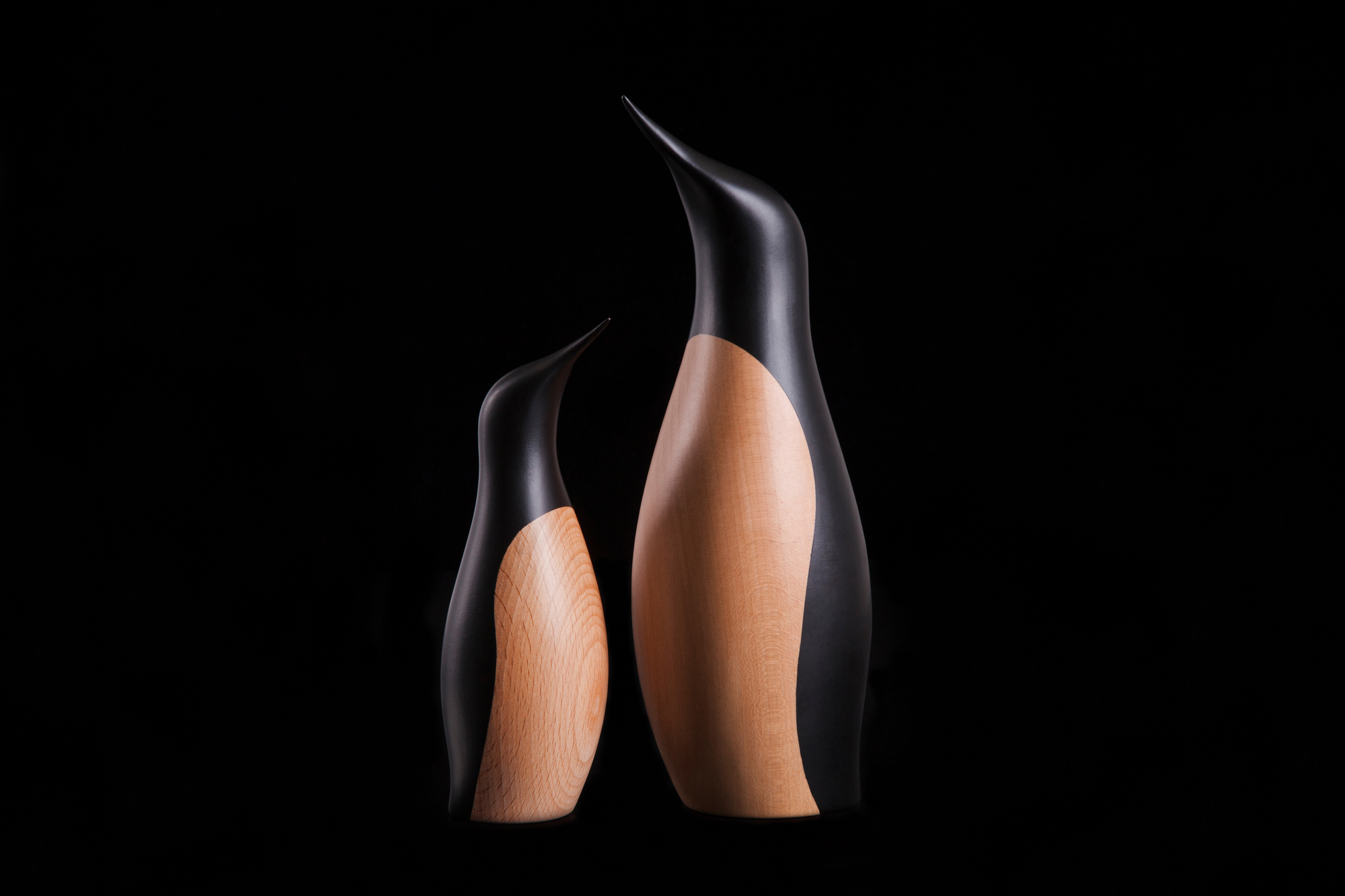 Zwei Pinguin Holzfiguren von Architectmade, eine kleine und eine große, auf schwarzem Hintergrund.