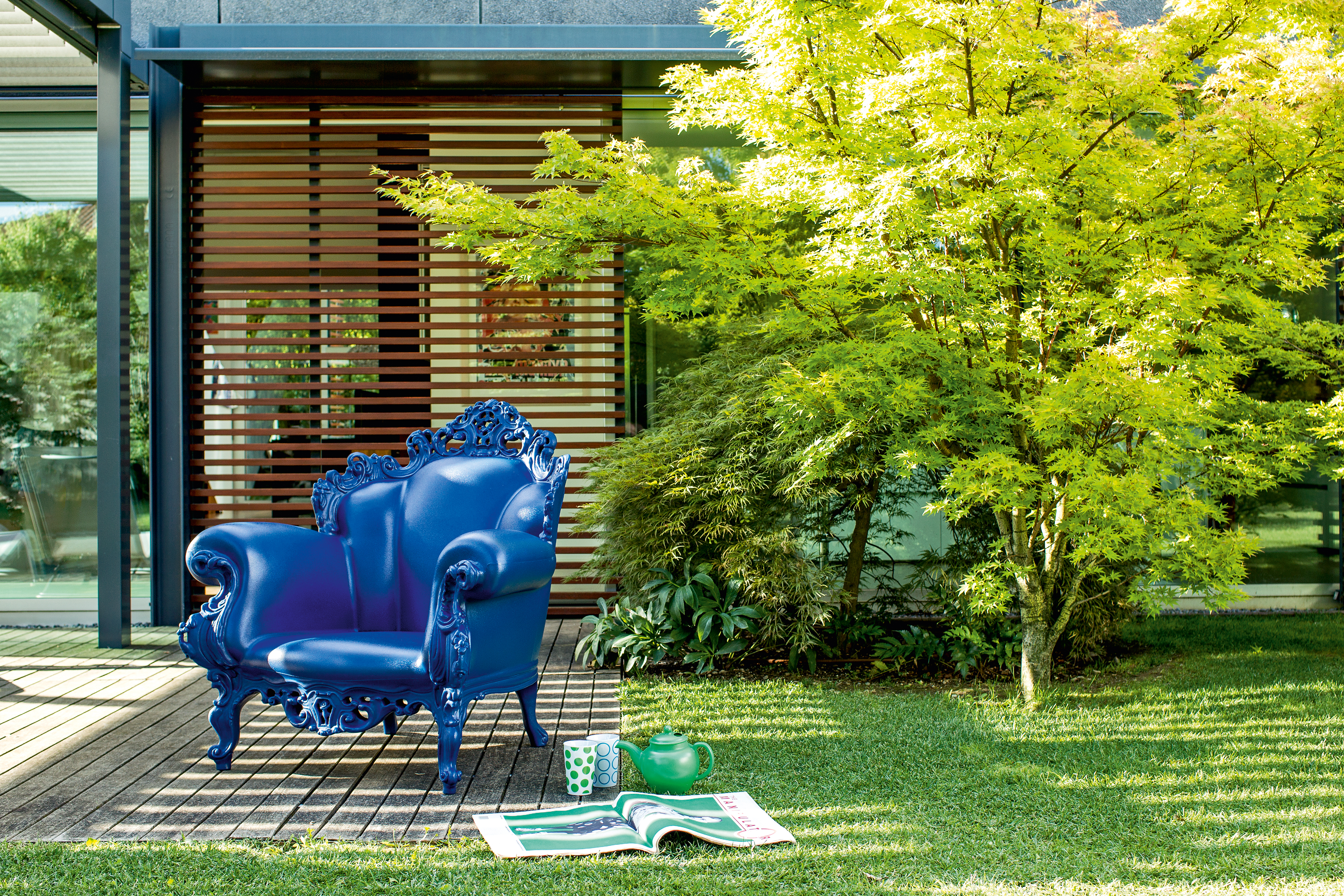 Blauer Magis Proust Sessel Outdoor auf Holzterrasse vor modernem Haus und Garten.