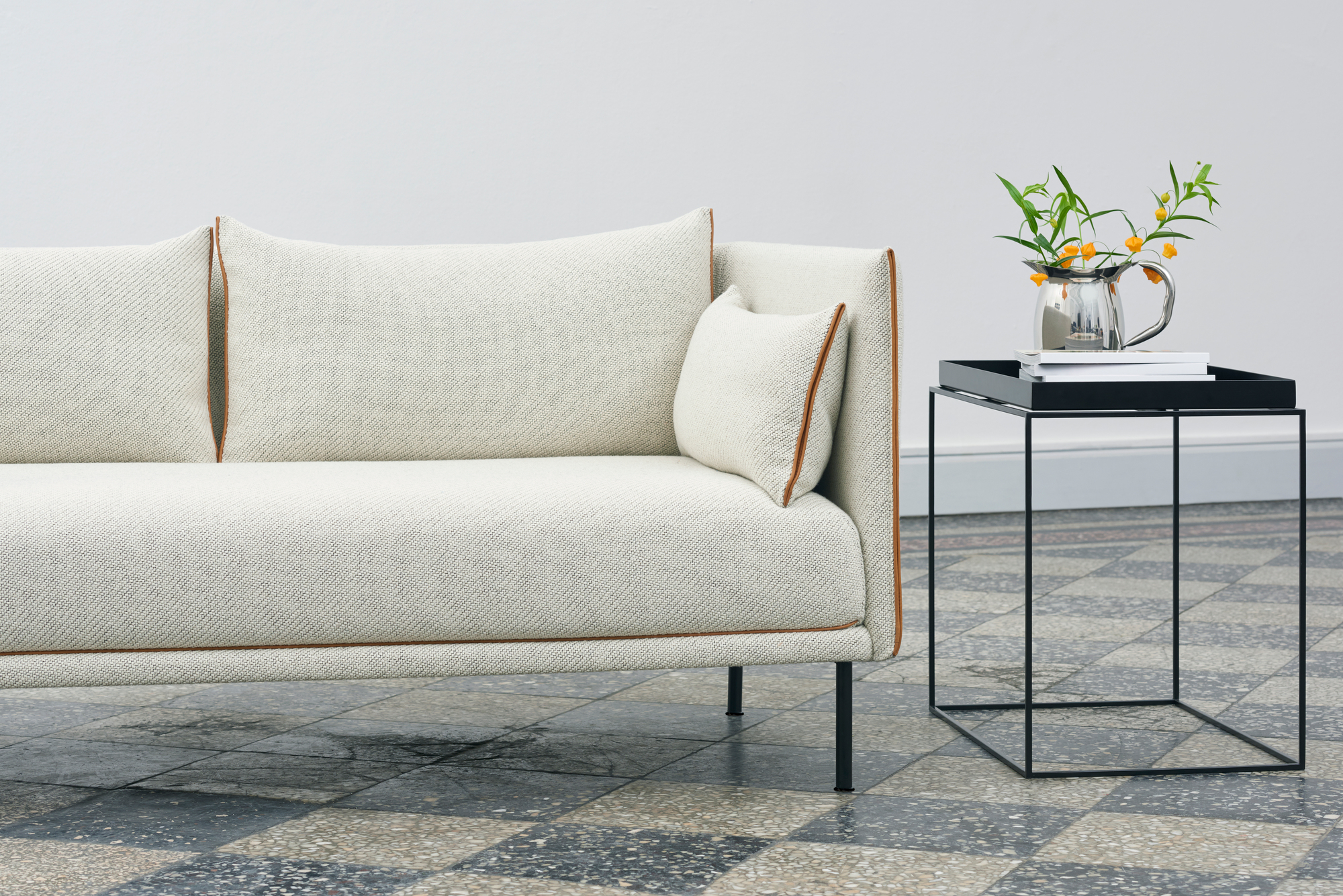 Heller Stoffsofa mit Zierkissen neben schwarzem Hay Tray Table L Beistelltisch mit Blumenvase.