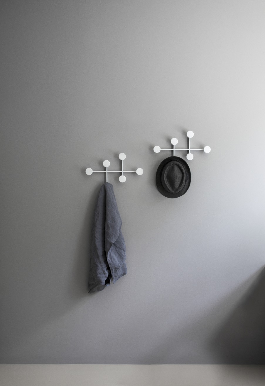 Afteroom Coat Hanger Medium: Zwei weiße Garderobenhaken mit Tuch und Hut an grauer Wand.