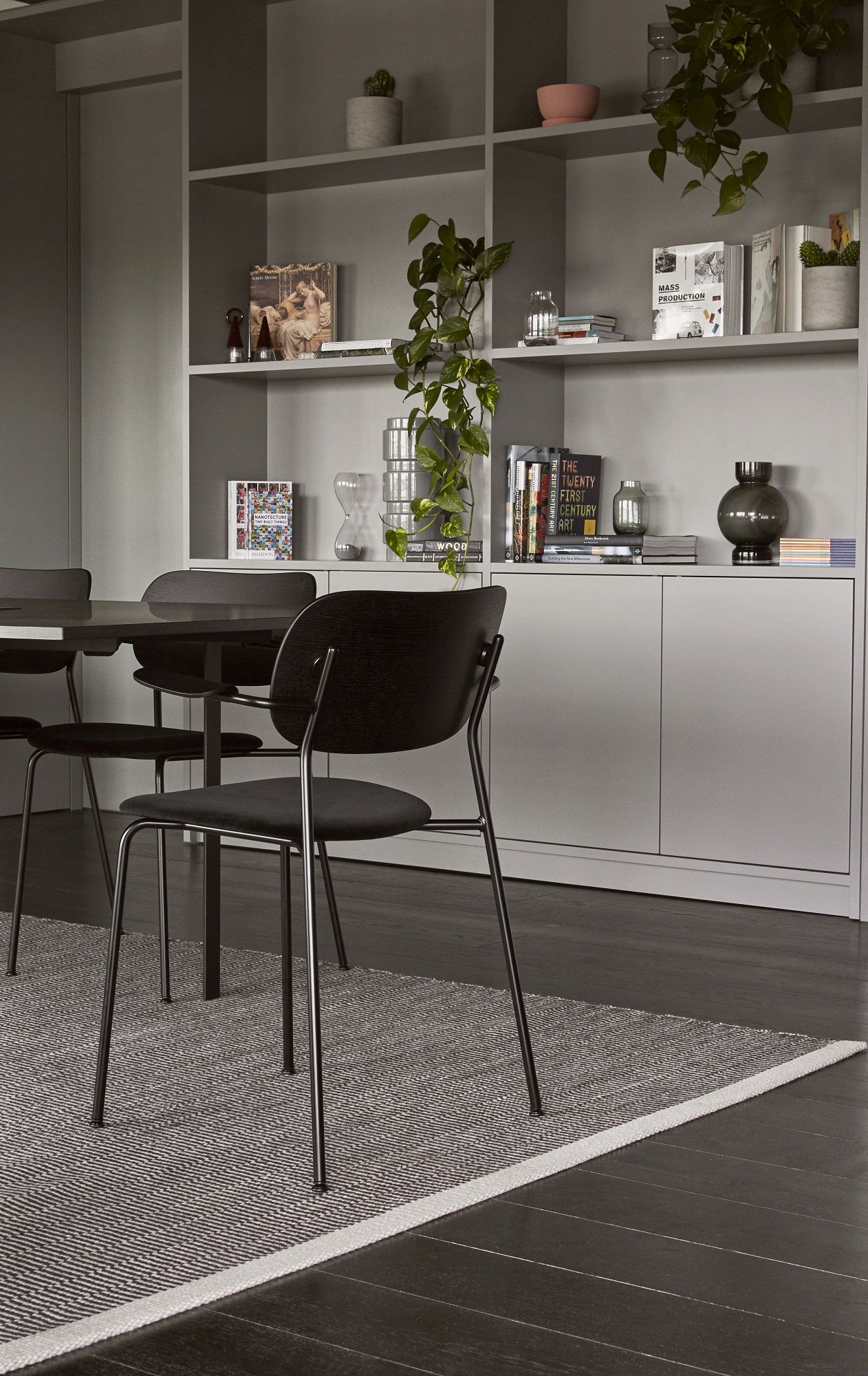 Schwarzer Co Dining Chair Stuhl von Audo Copenhagen am Esstisch vor Regalwand. Moderner Esszimmerstuhl mit Armlehne.