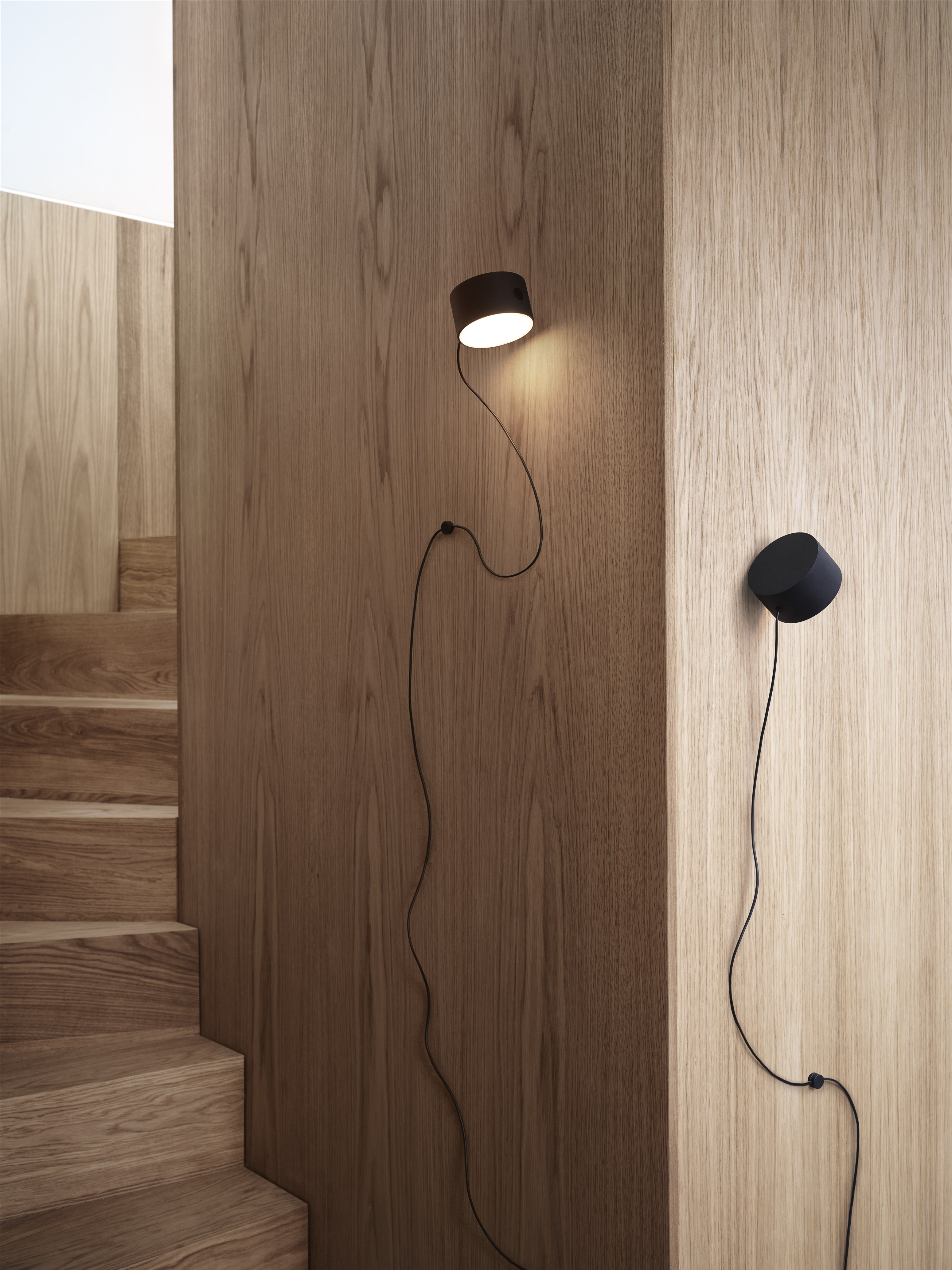 Zwei moderne, schwarze Wandleuchten mit Kabel an einer Holztreppe und Holzwand. Innenbeleuchtung.