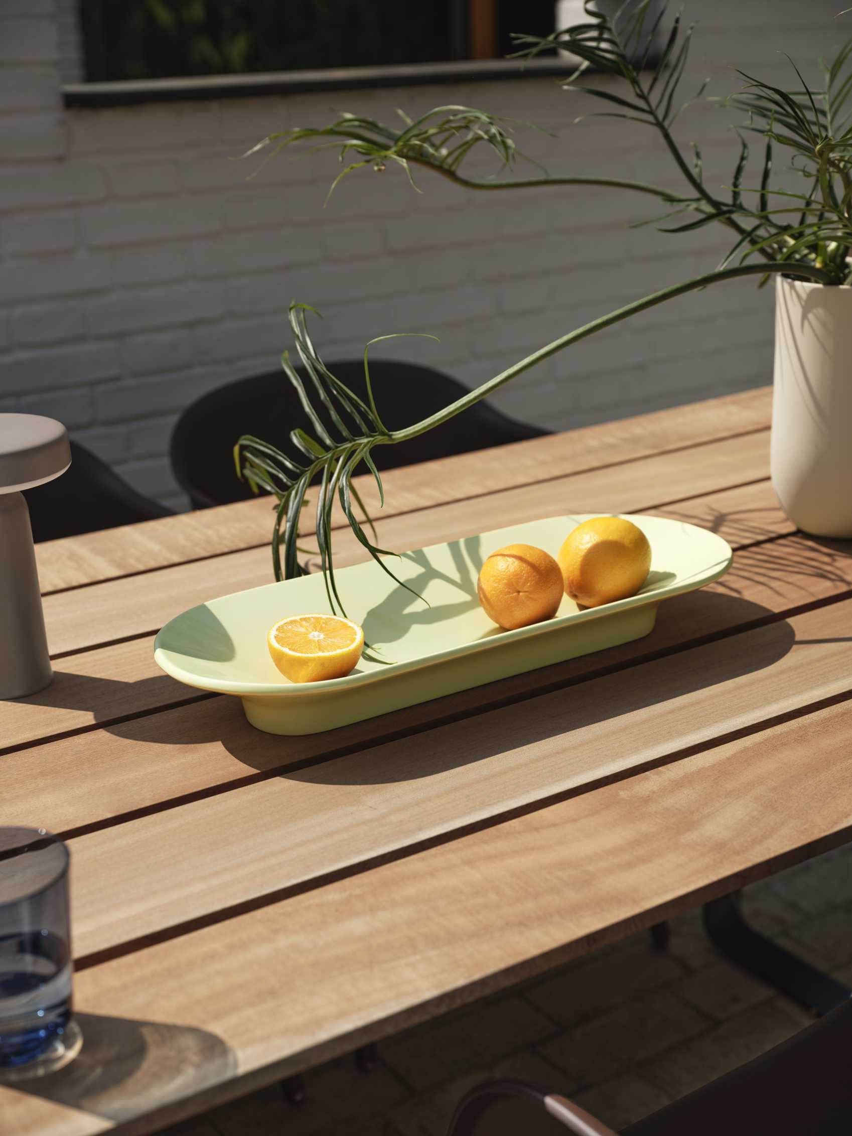 Nahaufnahme eines Fiber Outdoor Armlehnstuhls von Muuto an einem Holztisch mit Zitrusfrüchten.