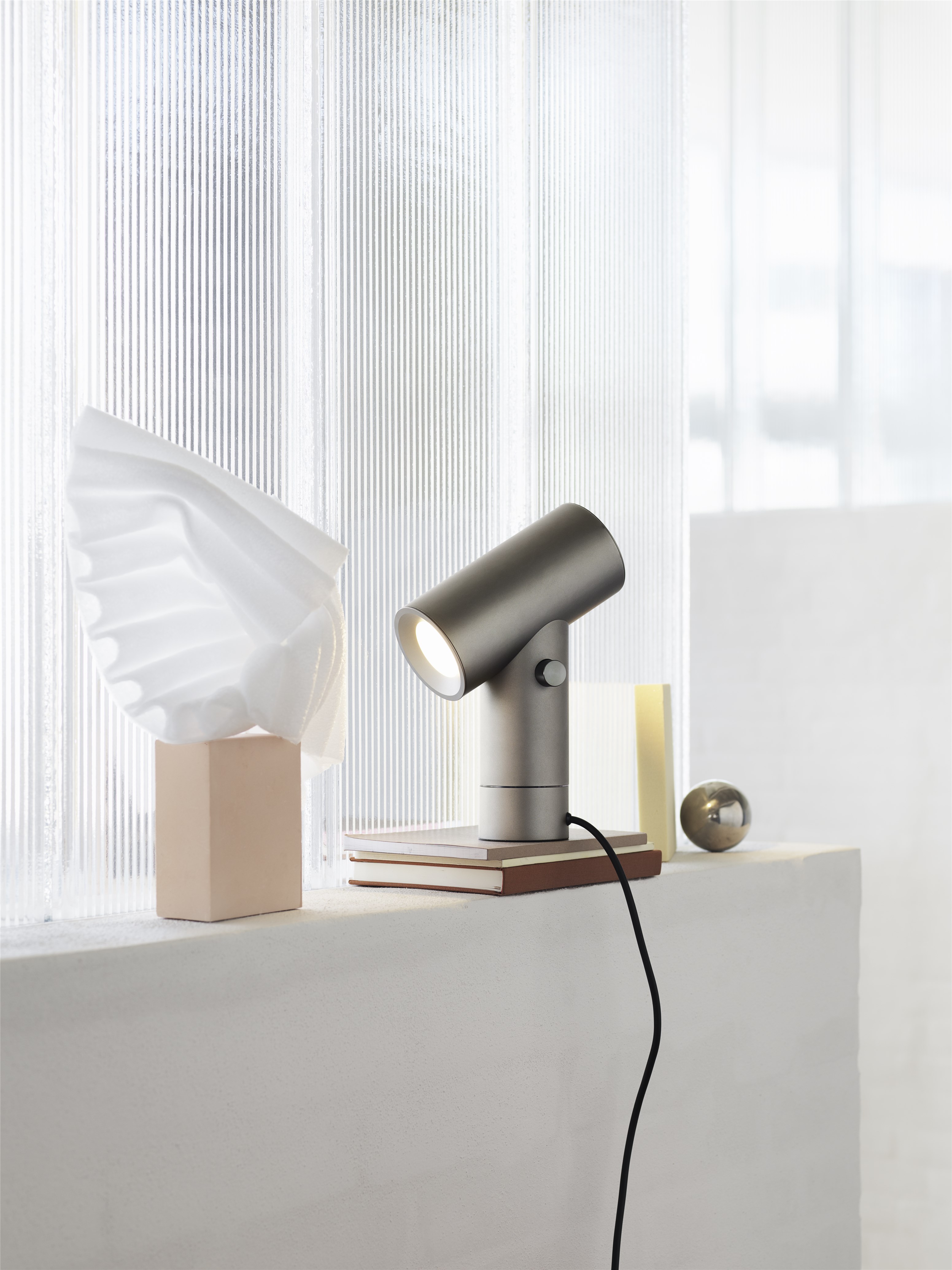 Moderne, graue Schreibtischlampe auf Büchern, mit minimalistischer Dekoration im Hintergrund. Design Lampe für Büro und Zuhause.