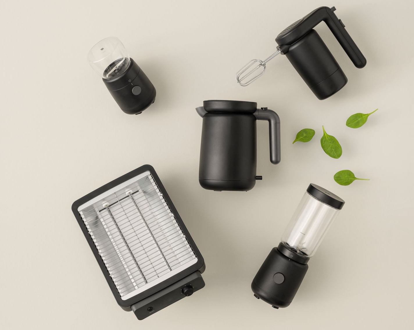 Schwarze Küchengeräte-Kollektion: Toaster, Wasserkocher, Handmixer, Smoothie-Maker und Gewürzmühle auf beigem Hintergrund.