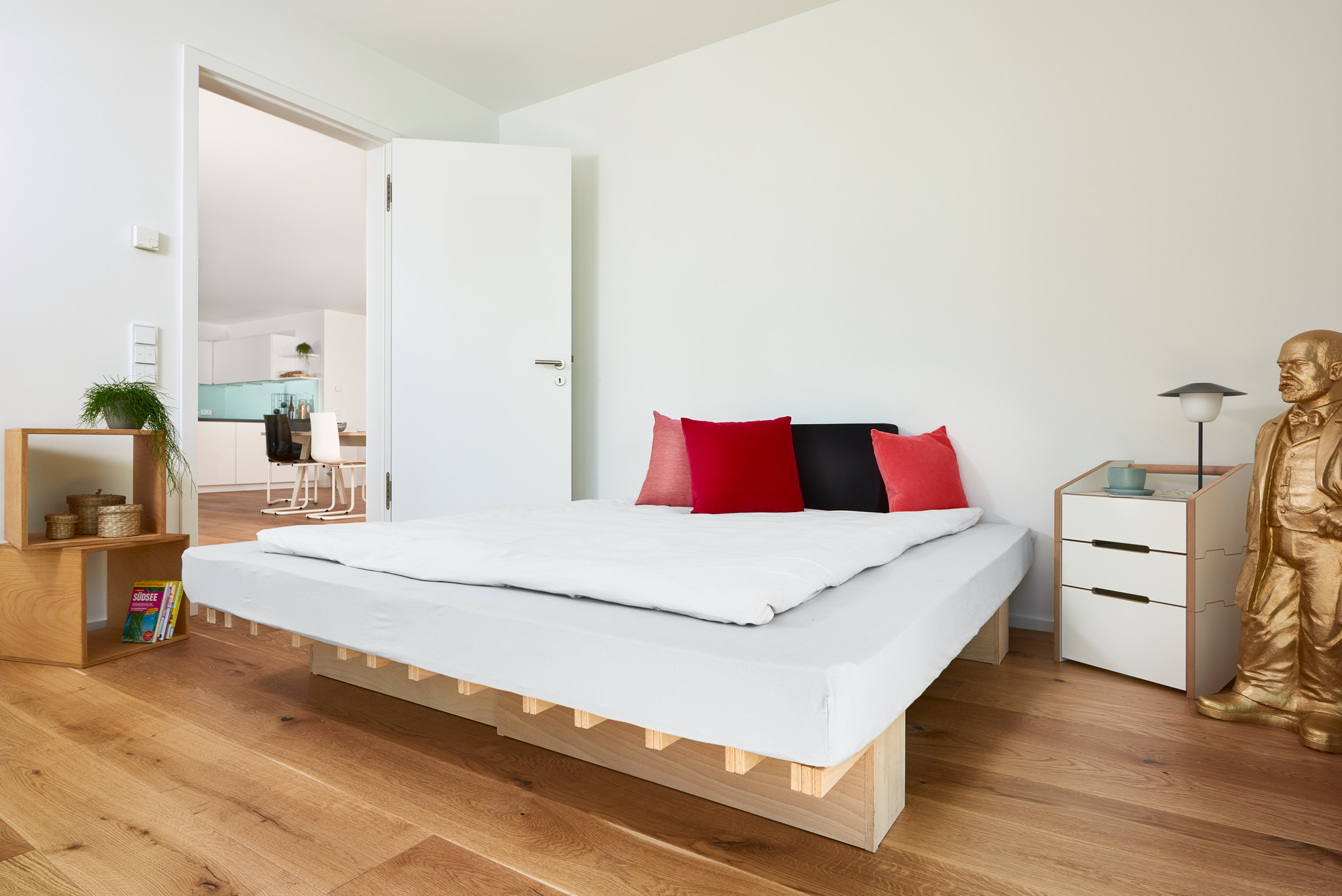 Tojo Ergo Faltmatratze im Schlafzimmer mit weißer Bettwäsche und farbigen Kissen auf Holzboden.