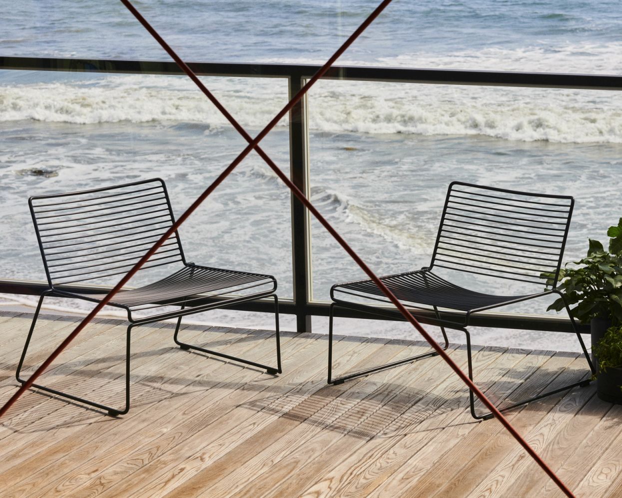 Zwei schwarze Hee Lounge Chairs von Hay auf einer Holzterrasse mit Meerblick. Design Gartenmöbel.