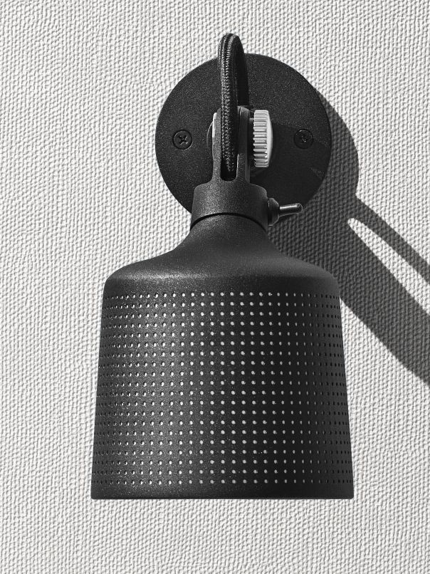 Schwarzer Vipp Wandspot mit perforiertem Schirm und Textilkabel an einer weißen Wand, Nahaufnahme für E-Commerce.