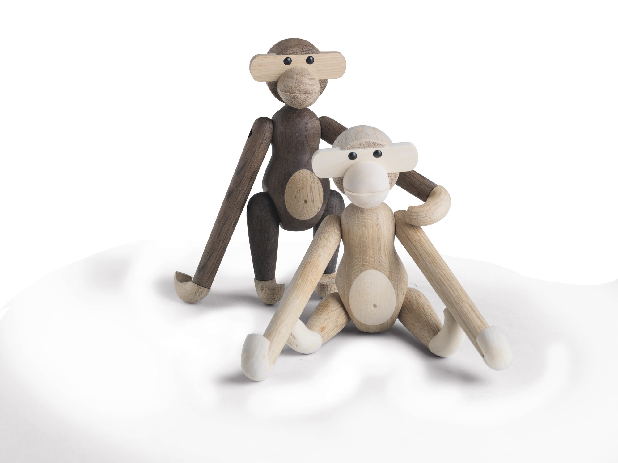 Zwei kleine Kay Bojesen Holzaffen, einer geräucherte Eiche, sitzen auf weißem Grund.