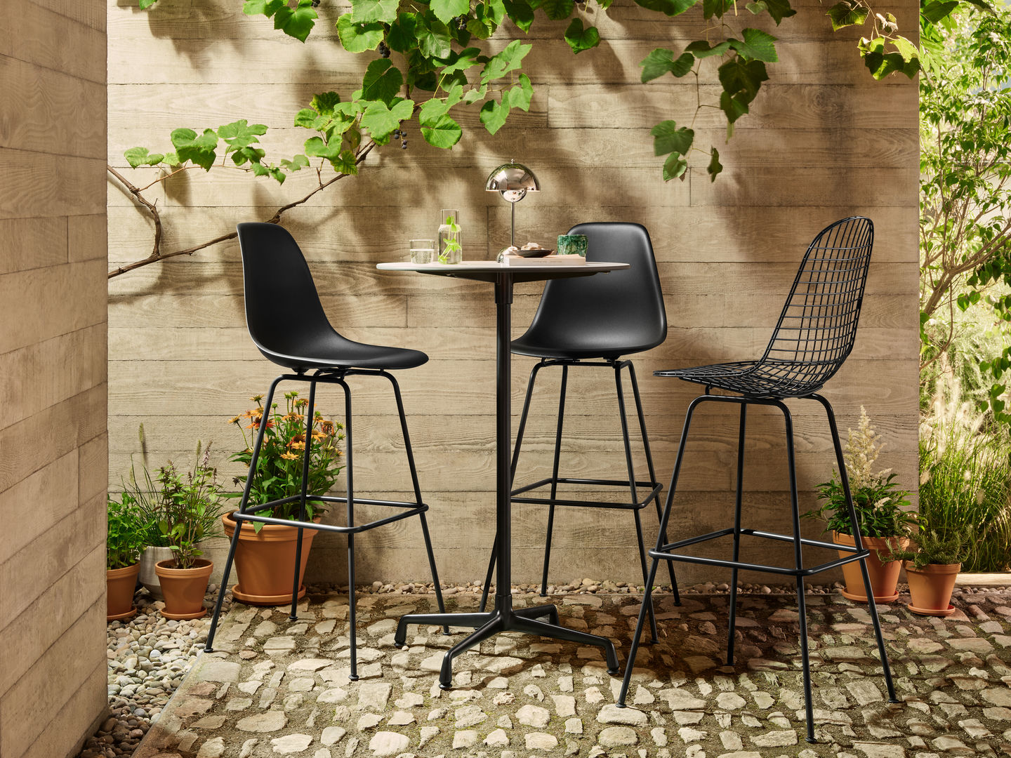 Eames Wire Bar Stool Barhocker High von Vitra, schwarzes Metallgestell mit Sitzpolster, im Garten.