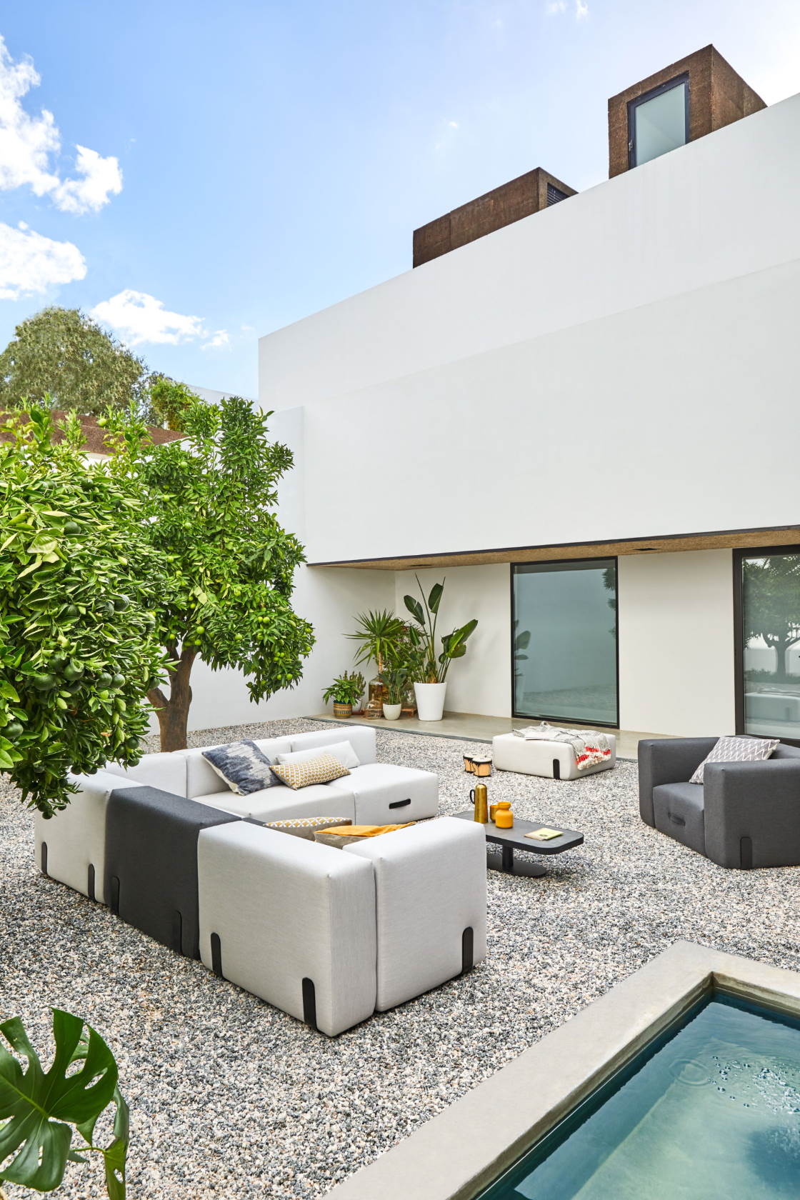 Helle Outdoor-Lounge mit modularem Sofa, Sessel und Beistelltisch im modernen Garten mit Pool.