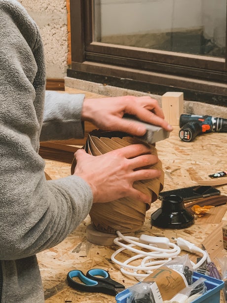 Mann schleift handgefertigte Holzlampe, DIY-Projekt für individuelle Lampen, nachhaltige Beleuchtung, handwerkliche Holzbearbeitung.