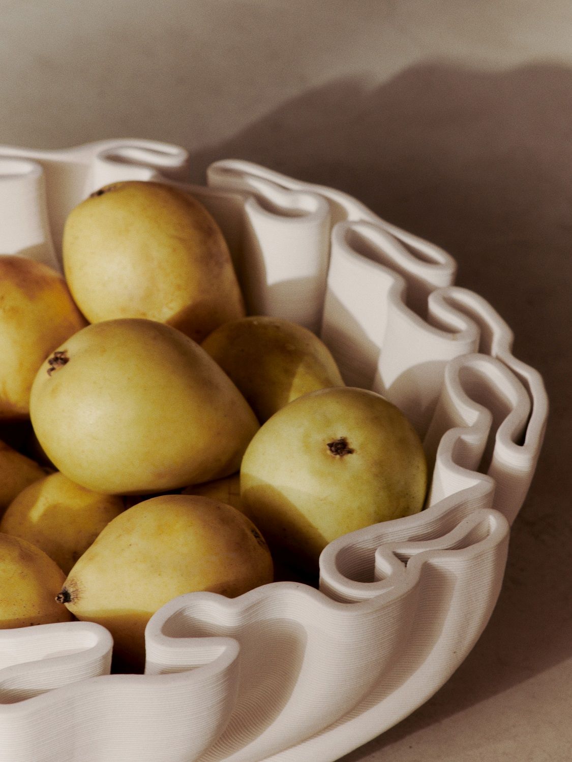 Nahaufnahme der Ferm Living Dedali Bowl Schale in Off-white, gefüllt mit reifen, gelben Birnen. Dekorative Obstschale für Küche und Esstisch.