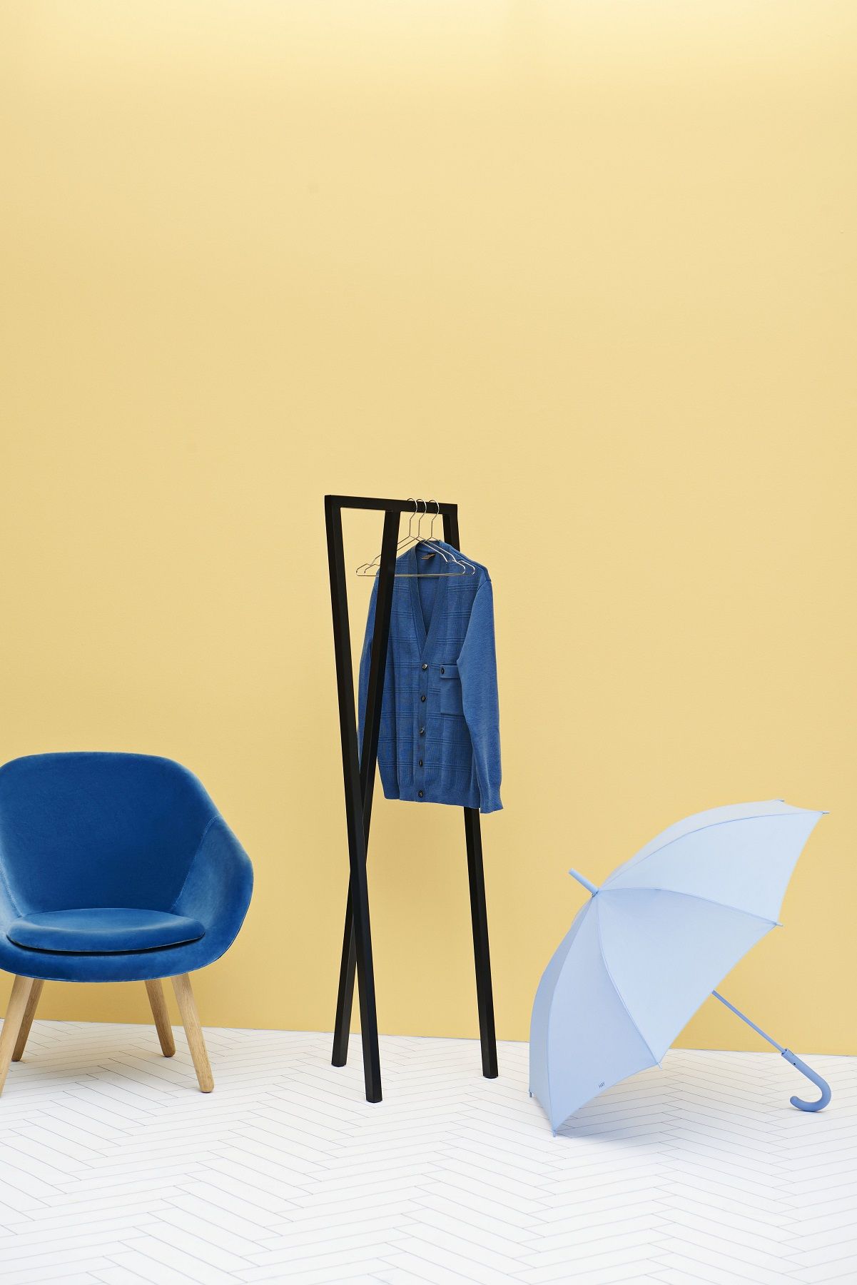 Hay Loop Stand Hall Garderobe in Schwarz mit Jacke, Stuhl und Schirm vor gelbem Hintergrund.