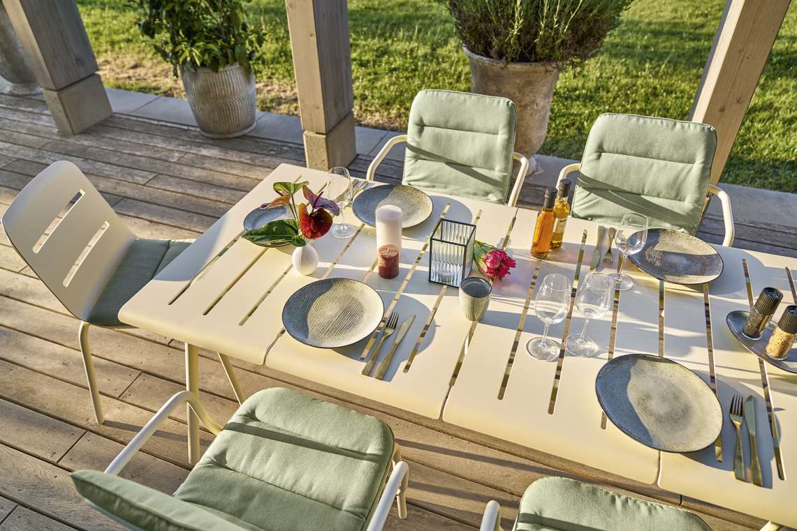 Vapio Tisch von Weishäupl, ein stilvoller Outdoor-Esstisch mit Stühlen und gedecktem Tisch auf einer Terrasse.