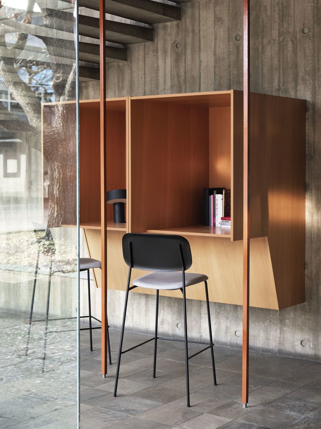 Hay Soft Edge 90 Bar Stool Low mit schwarzem Gestell und grauem Sitz vor Holzwand.