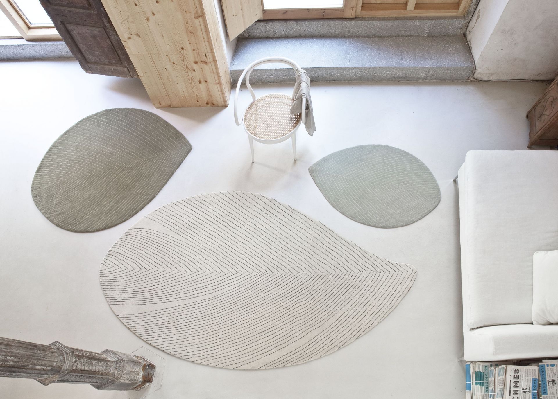 Drei moderne Teppiche in Blattform, beige und grau, im hellen Wohnzimmer mit Stuhl und Sofa.