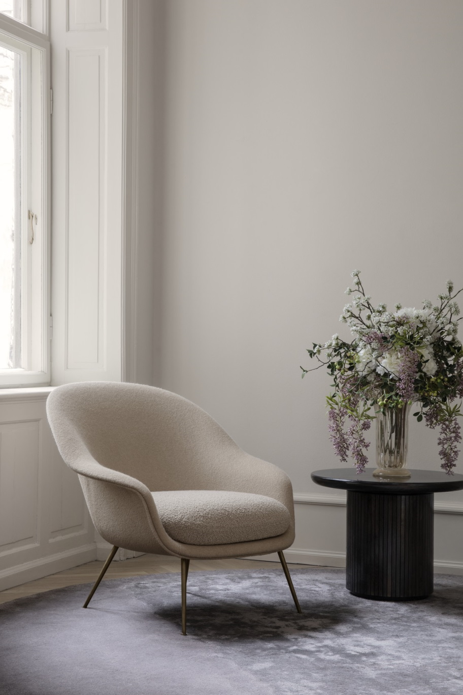 Beiger Sessel mit Gubi Moon Coffee Table Couchtisch und Blumenstrauß in stilvollem Interieur.