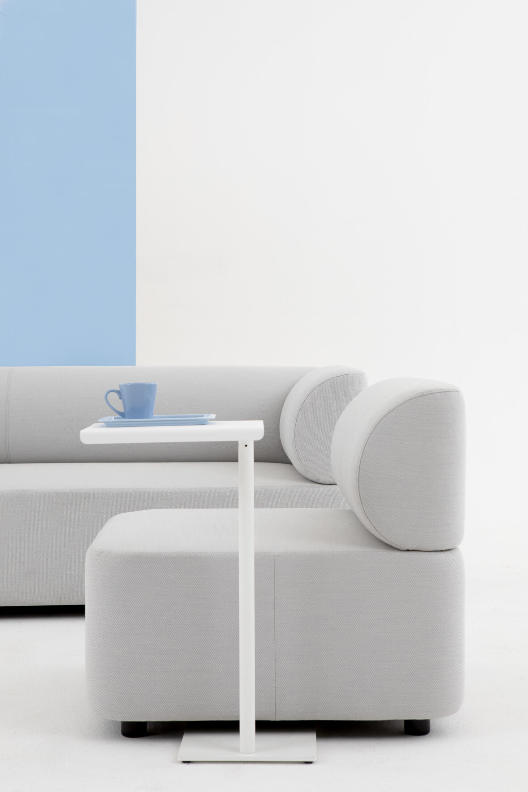 Mezza Sitzelement Sofa von Cascando in hellgrau mit Beistelltisch und blauer Tasse.
